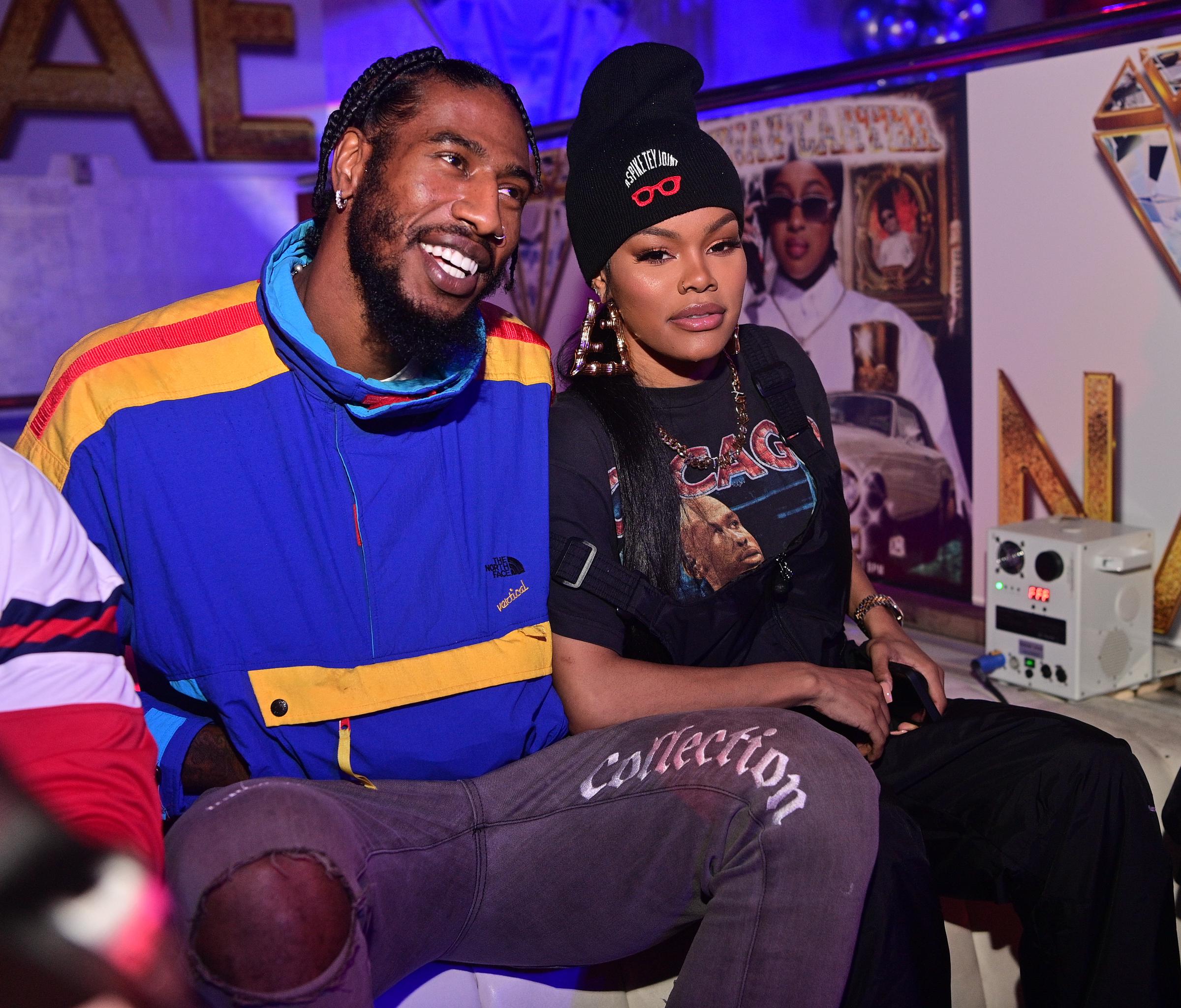 Iman Shumpert and Teyana Taylor pose together at Reginae Carter's 22nd birthday in Atlanta on November 29, 2020. Iman smiles in a bold blue-and-yellow jacket while Teyana sits beside him in a black beanie and graphic top.
