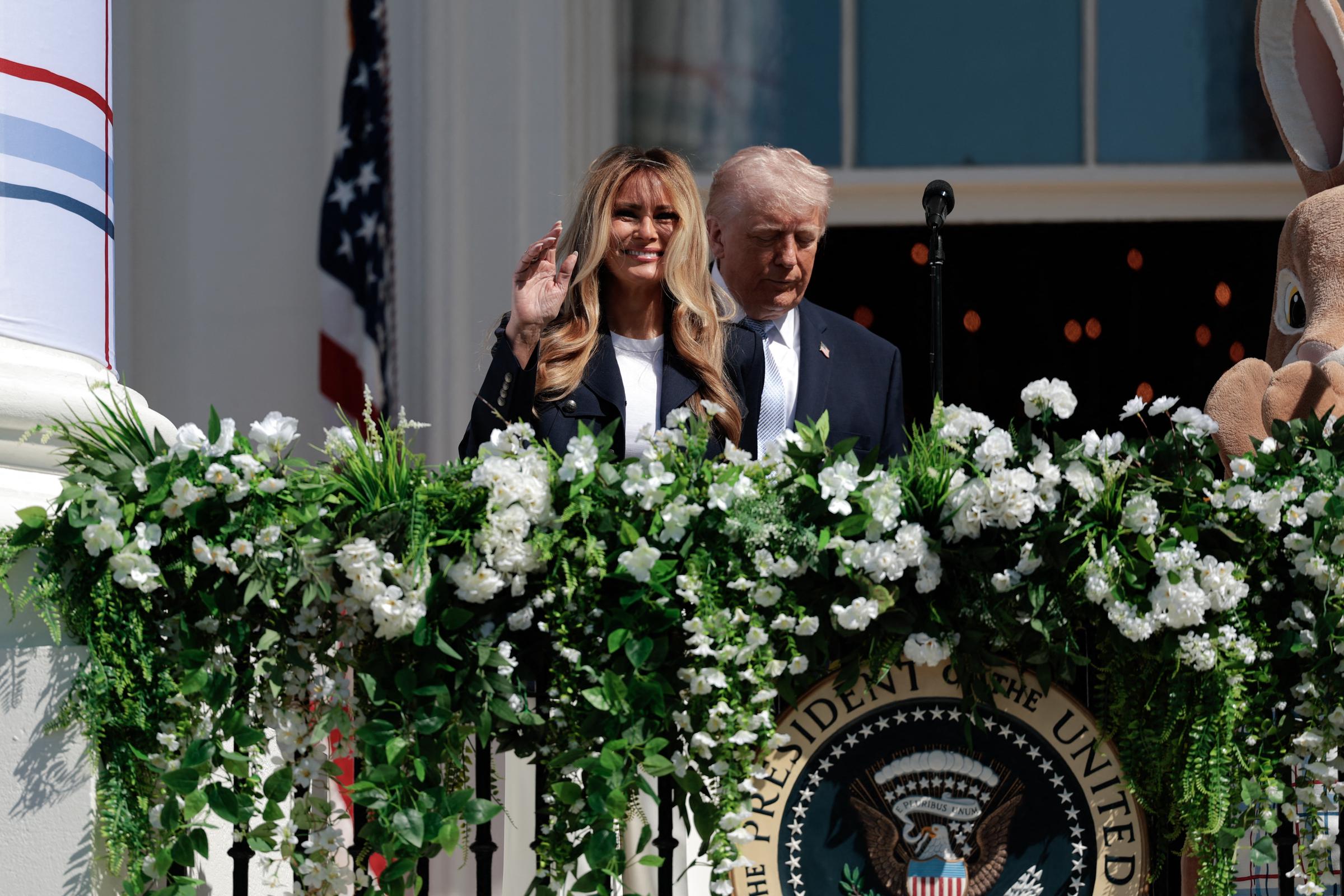 Melania Trump smiles and waves from the White House balcony while Donald Trump stands behind her during the Egg Roll, a springtime tradition held on the South Lawn.