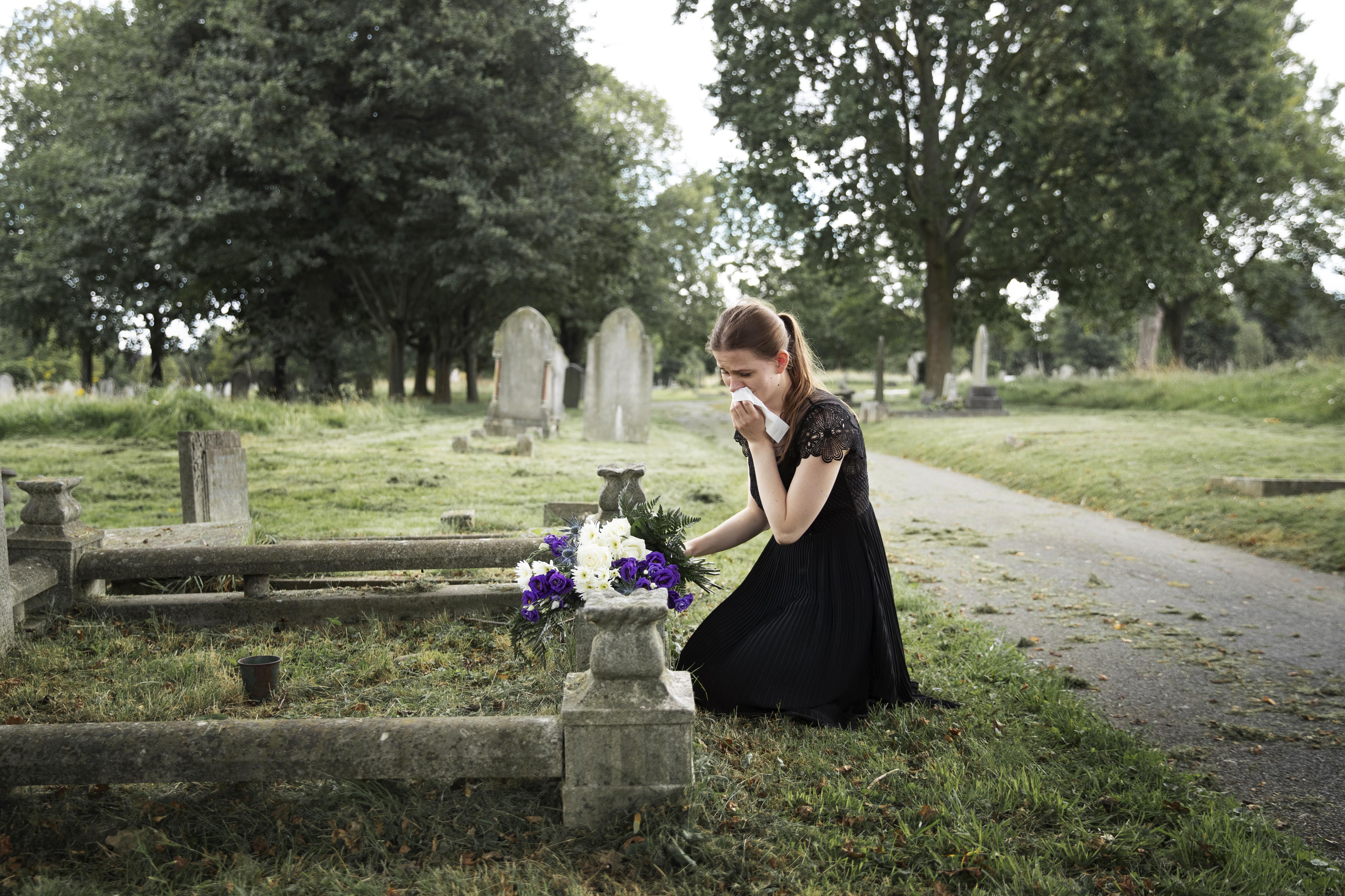 A young woman mourning beside the grave of a loved one | Source: Freepik