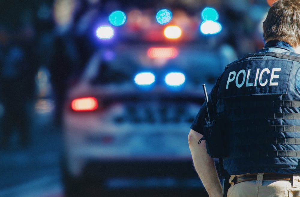 Ein amerikanischer Polizist geht auf der Straße, im Hintergrund ist ein Polizeiauto zu sehen | Quelle: Shutterstock/ALDECA studio