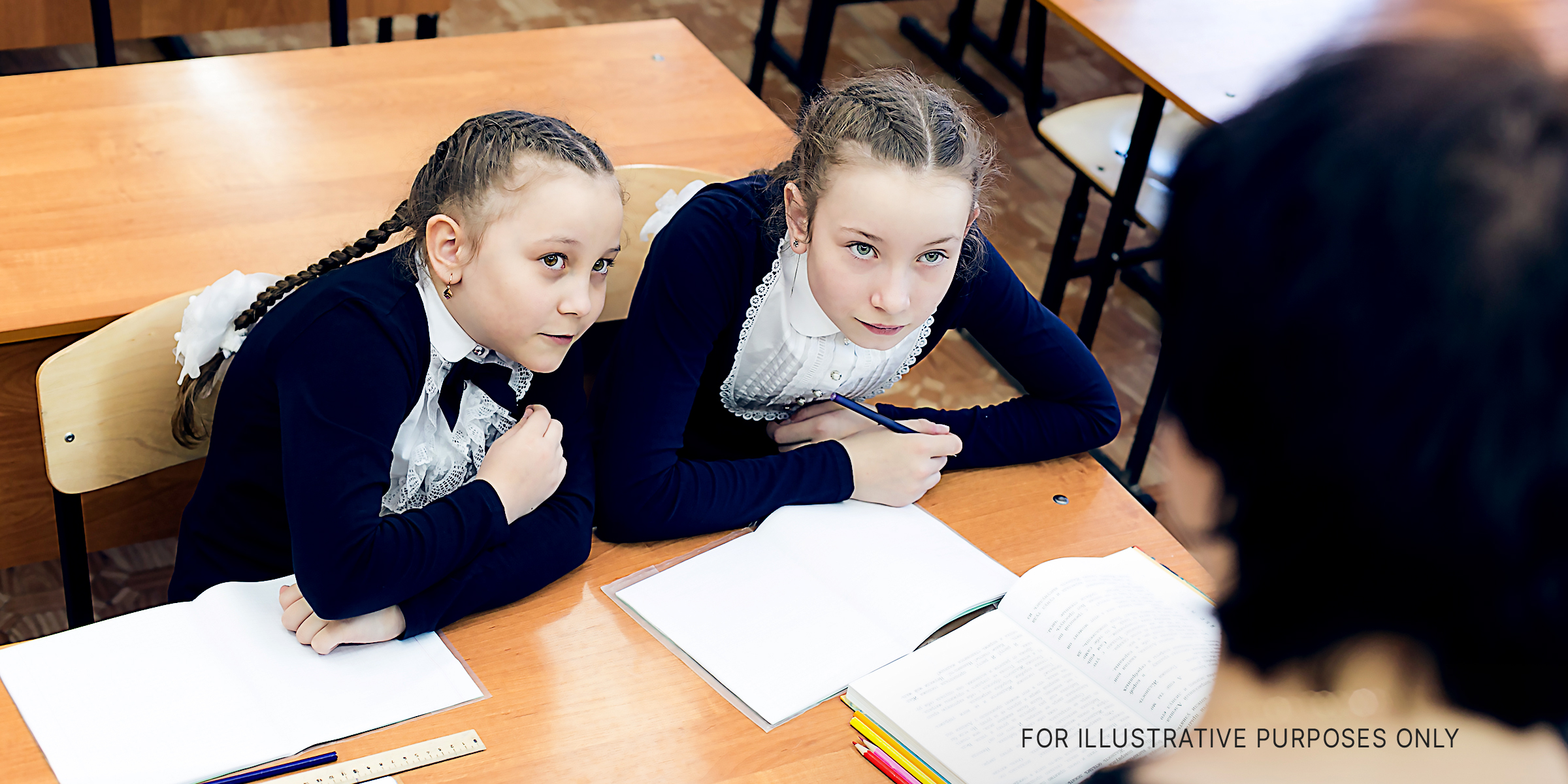 Two schoolgirls looking at a person standing in front of their desk | Source: Shutterstock