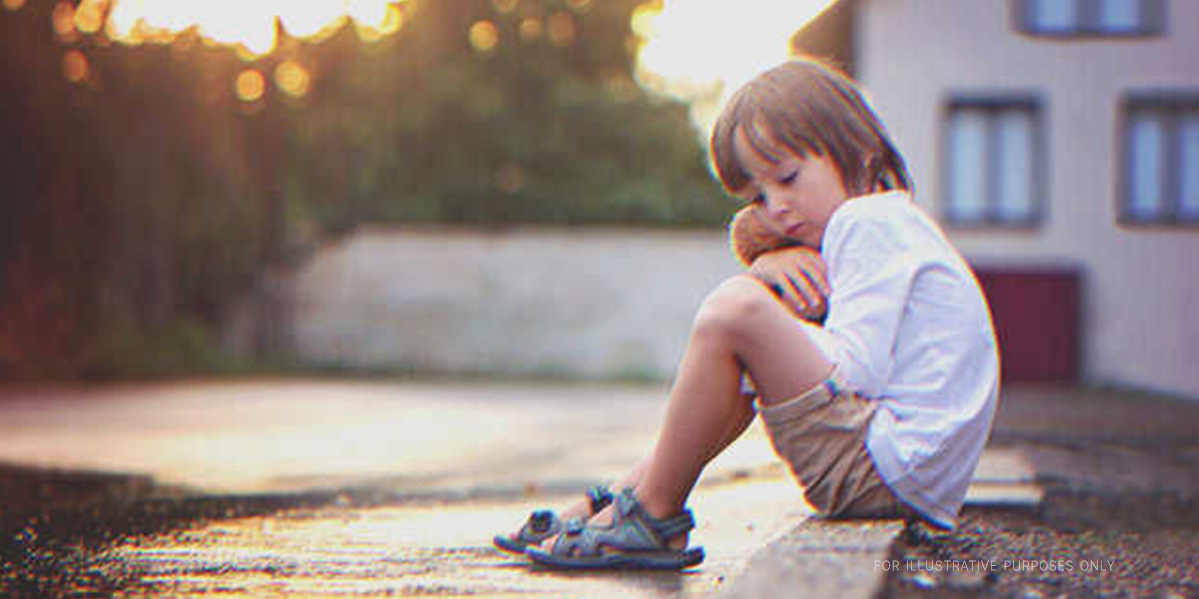 Boy sitting on a sidewalk looking sad. | Source: Shutterstock