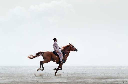 Photo of a man riding a horse on sand against a clear sky | Photo: Getty Images