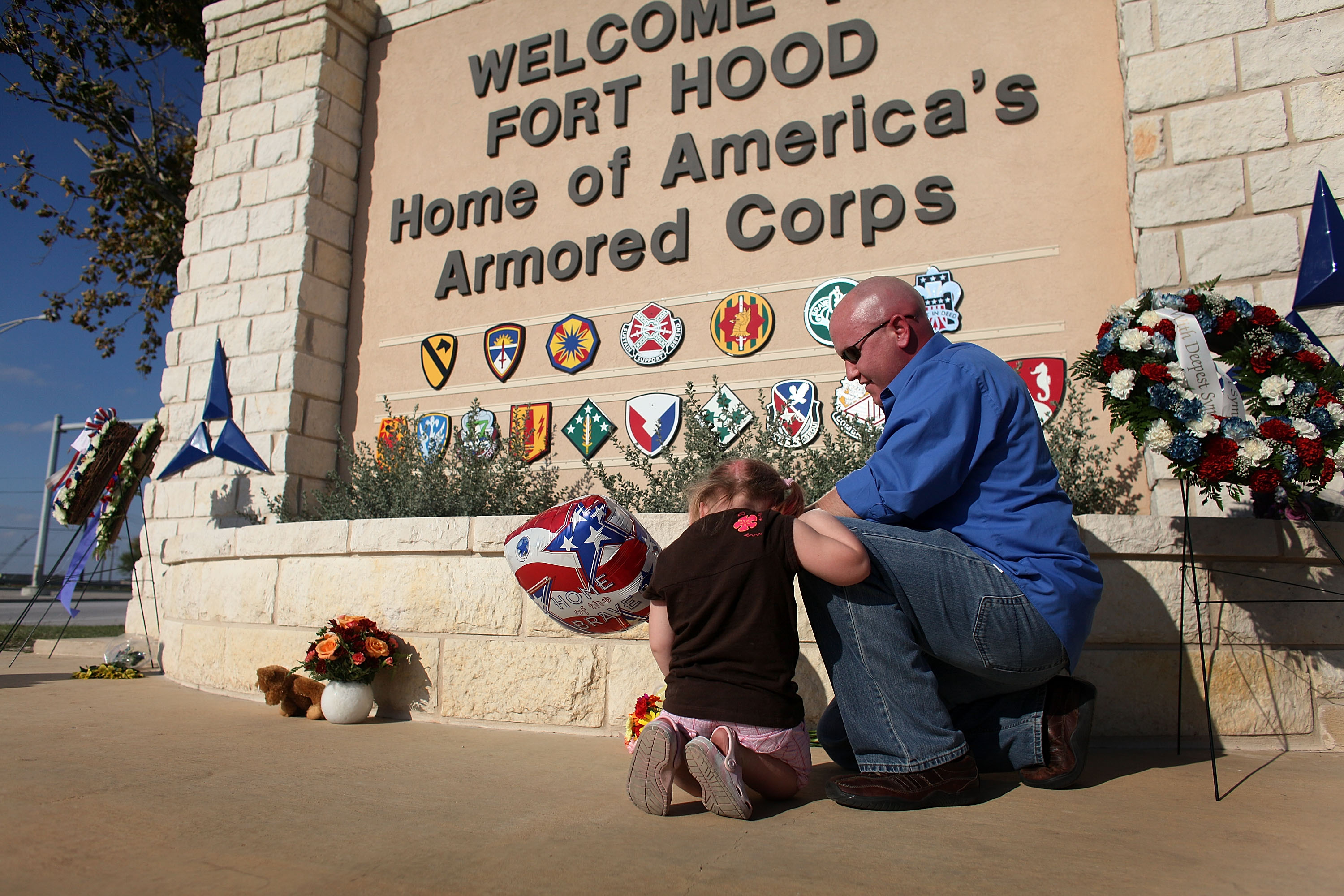 U.S. Army Specialist Ryan Hill and his daughter, Emma Hill, pray together as they light a candle and lay flowers at the front gate to Fort Hood following a shooting rampage on the grounds on November 7, 2009, in Killeen, Texas | Source: Getty Images