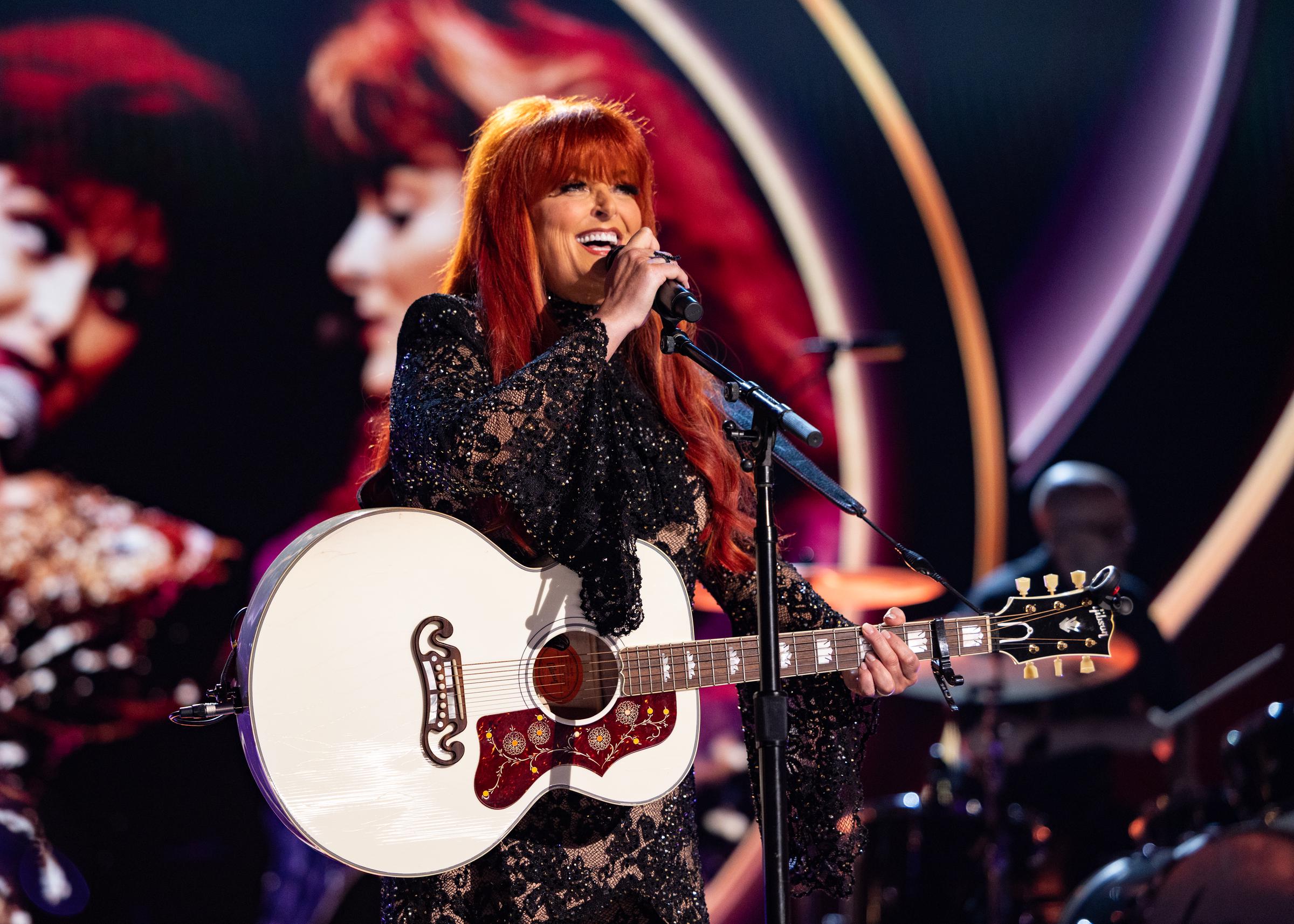 Wynonna Judd performs with a smile during the 60th ACM Awards at the Ford Center in Frisco, Texas. Her sparkling outfit, signature red hair, and heartfelt vocals lit up the stage in a memorable musical moment.