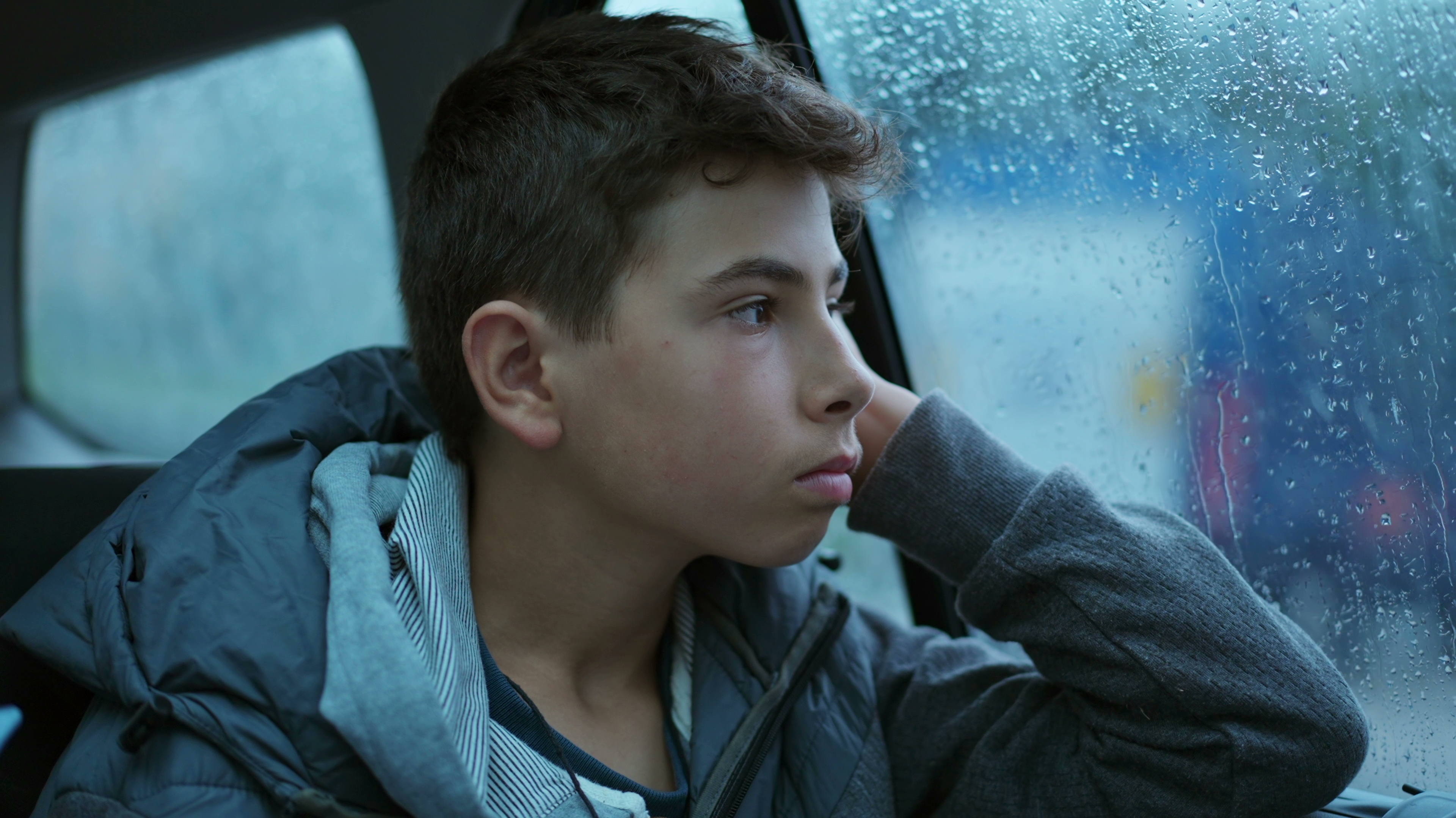 Thoughtful young boy seated in car backseat staring at glass window looking at landscape passing by. | Source: Shutterstock