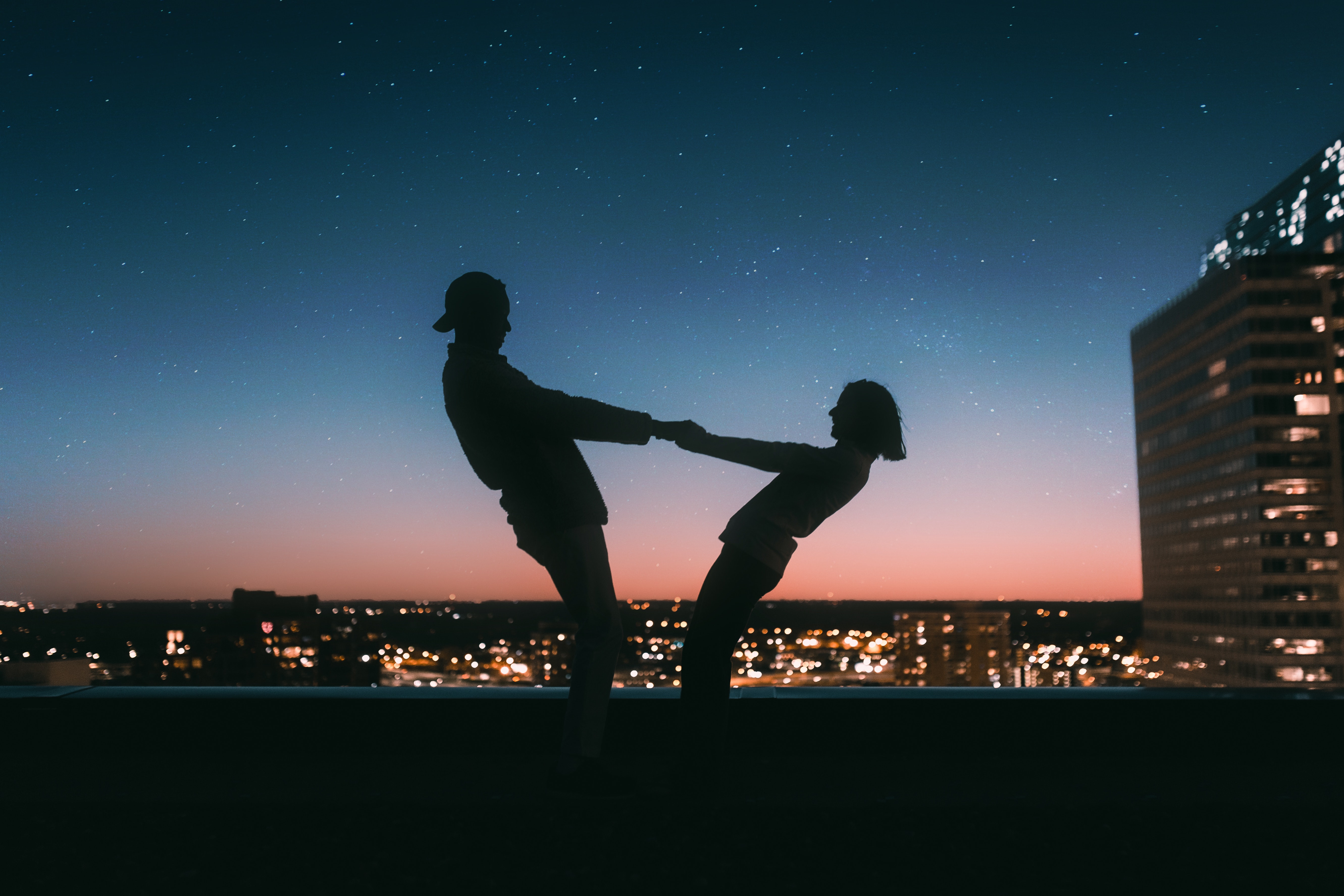 A silhouette of two individuals having fun on a roof in a city. | Source: Pexels