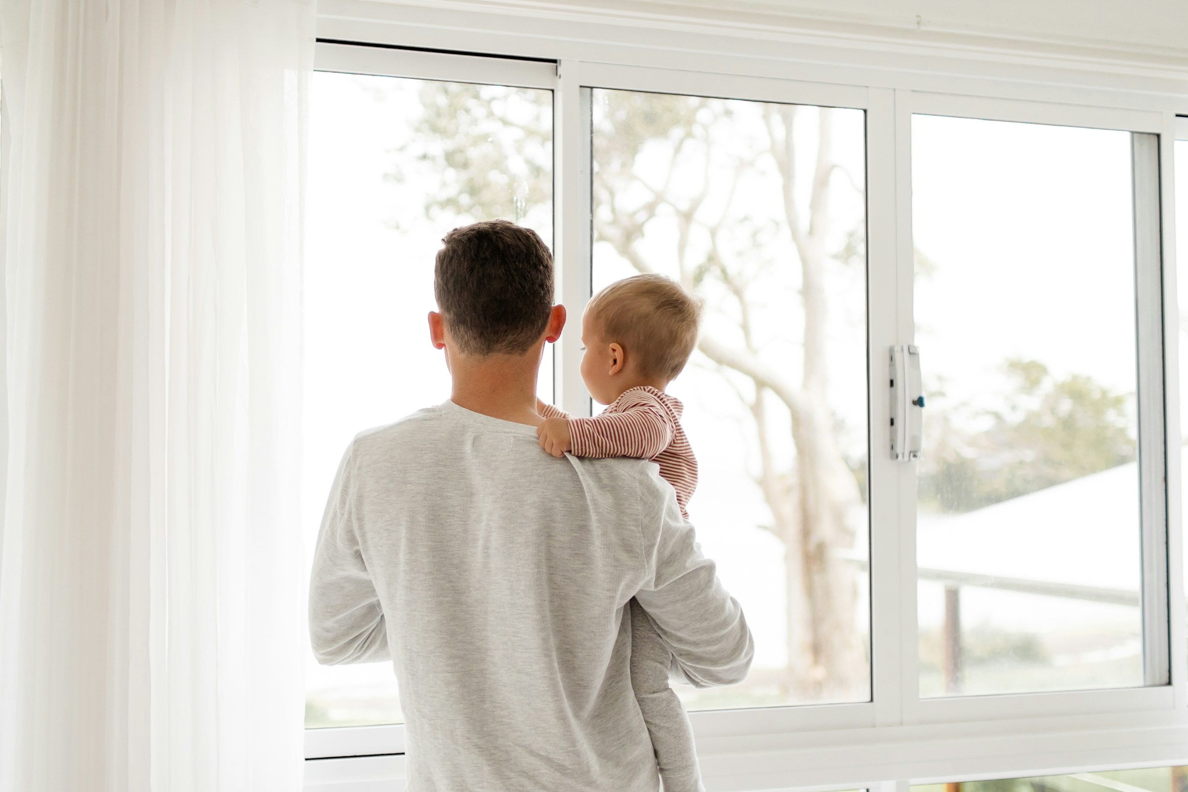 A man holding a baby looking through the window | Source: Pexels