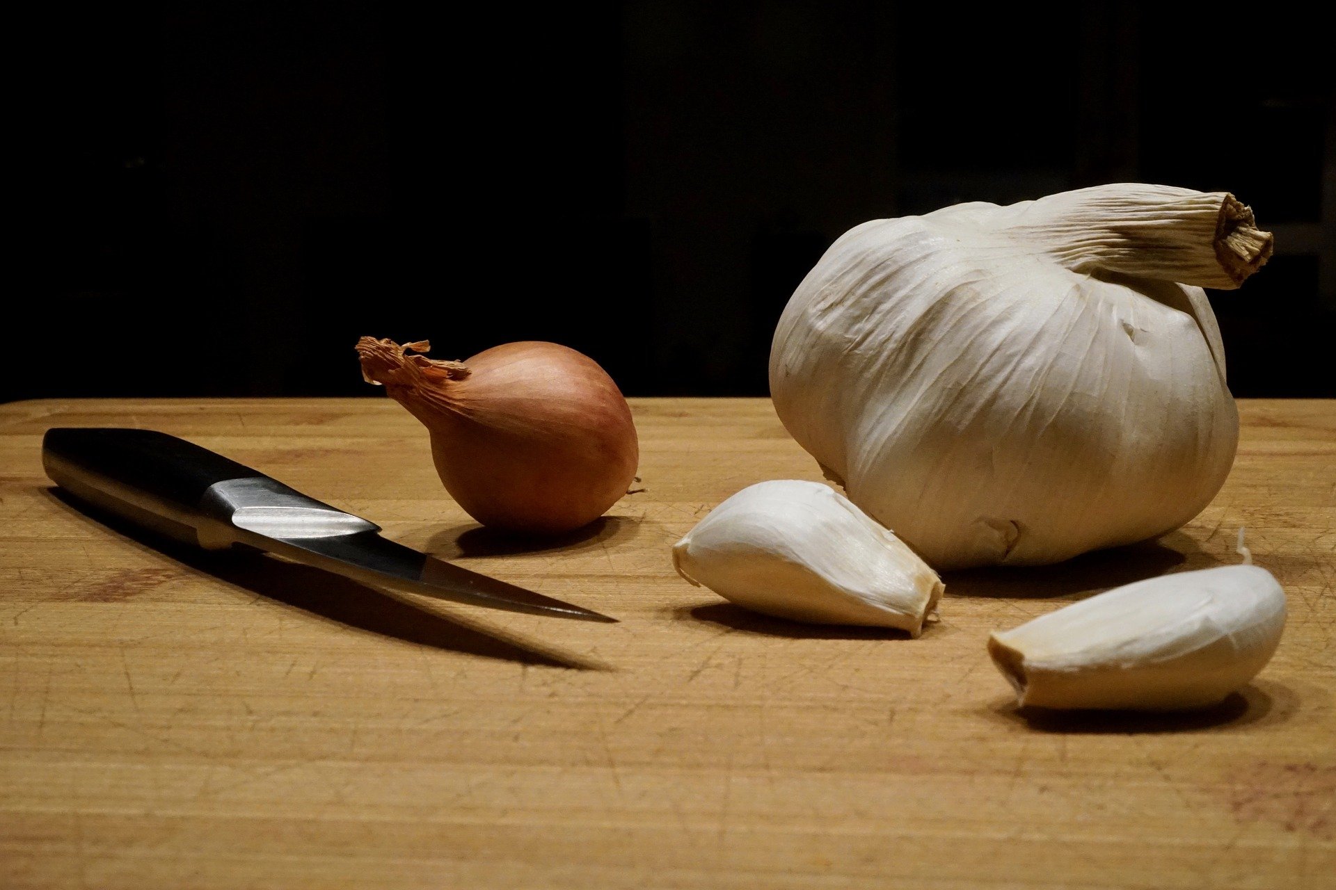 Dientes de ajo, cabeza de ajo y cuchillo sobre tabla de cortar. | Foto: Pixabay