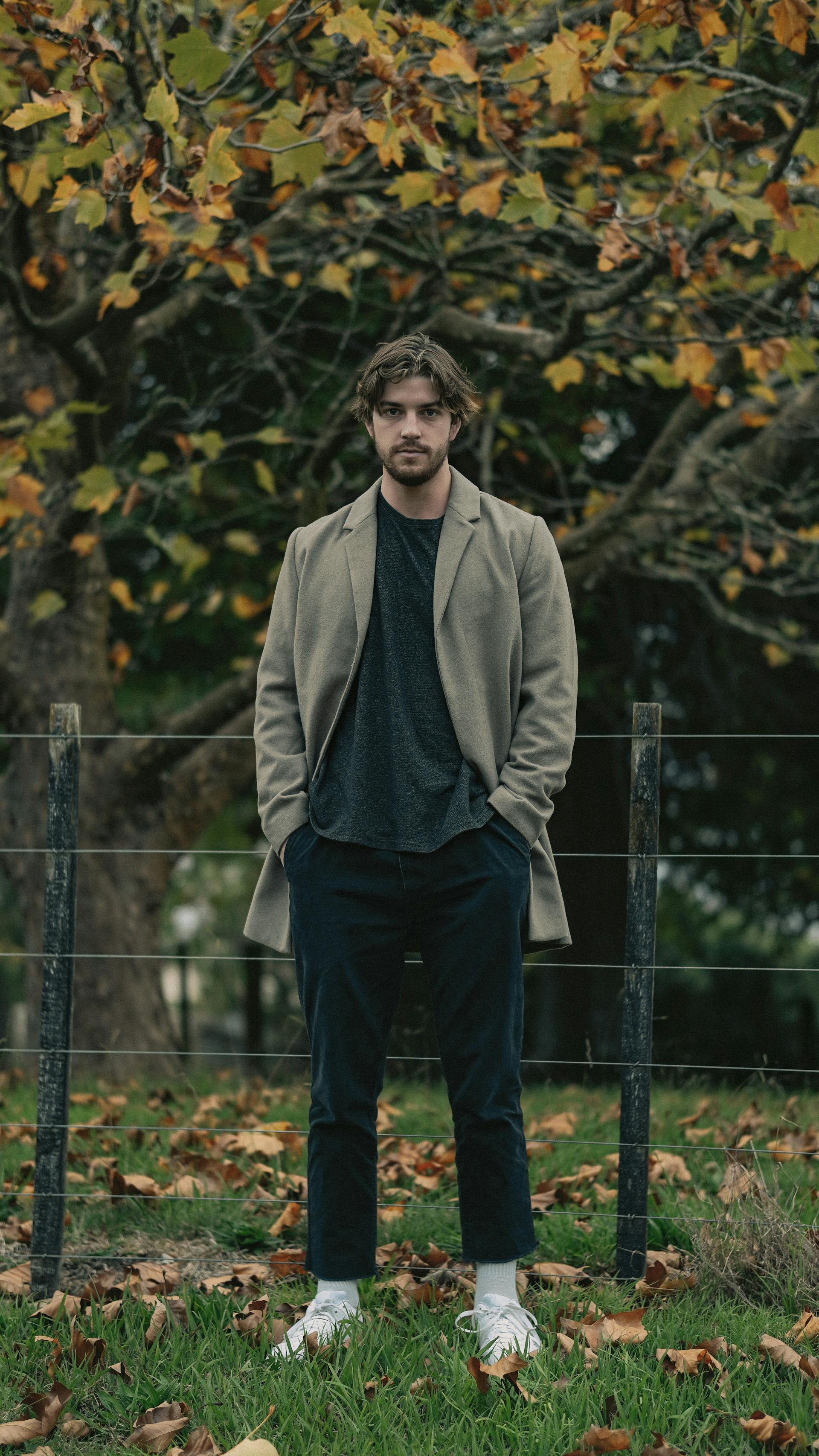 A man in a brown coat standing beside a wooden fence | Source: Pexels