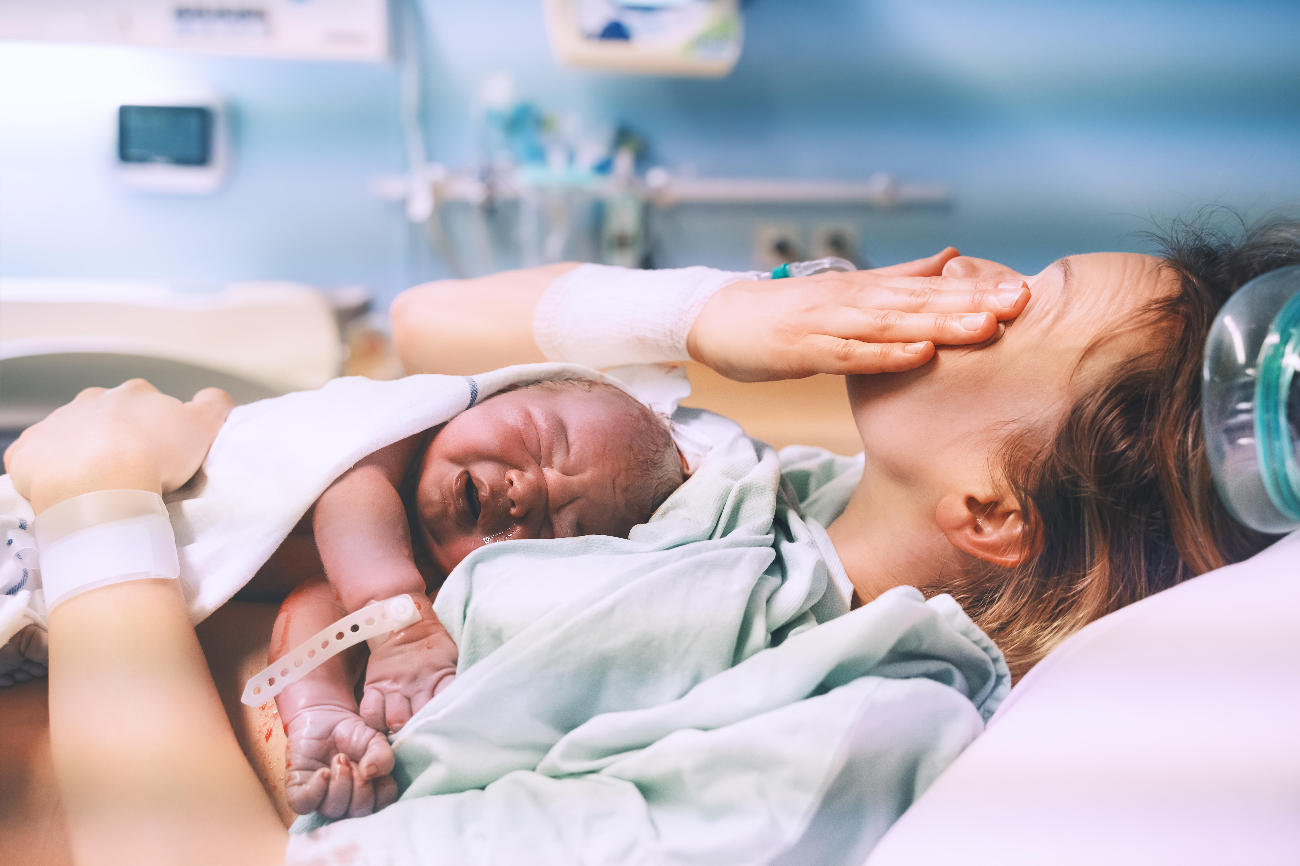 A young mother wipes her tears away while hugging her newborn baby after giving birth | Source: Shutterstock