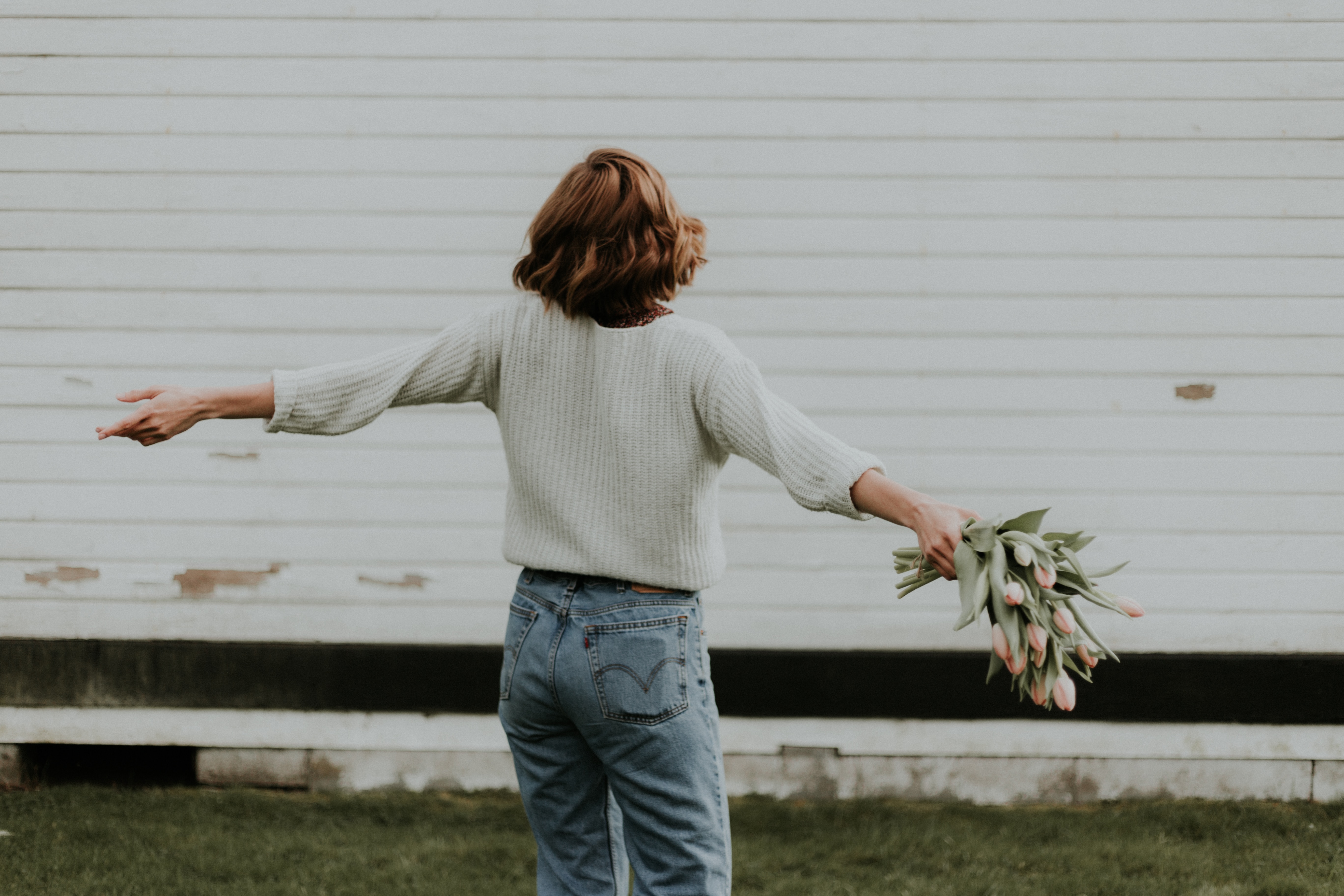 A woman spreading her arms while holding flowers.│Source: Unsplash