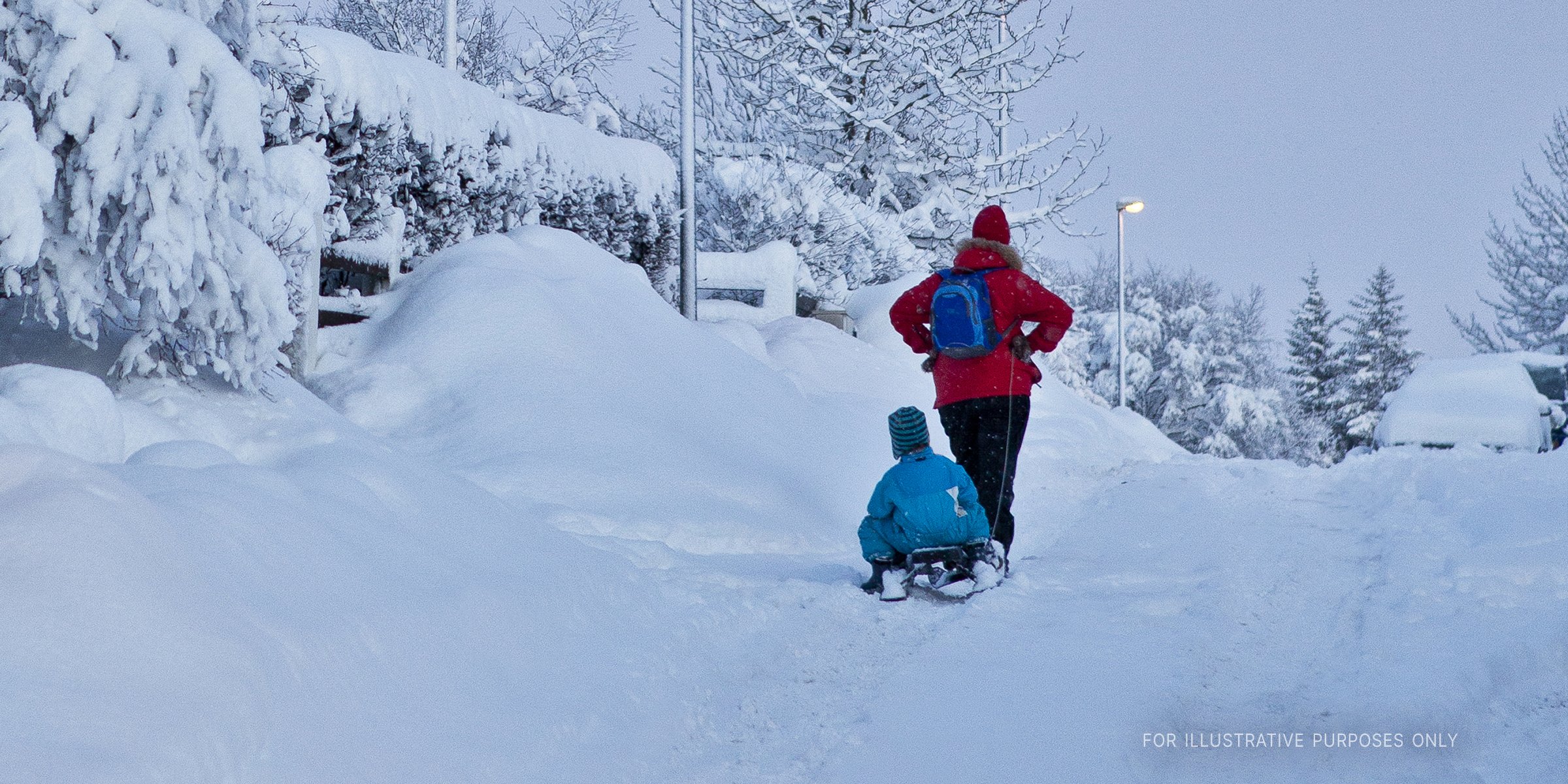 Adult carrying a kid in a snow sled | Source: Shutterstock