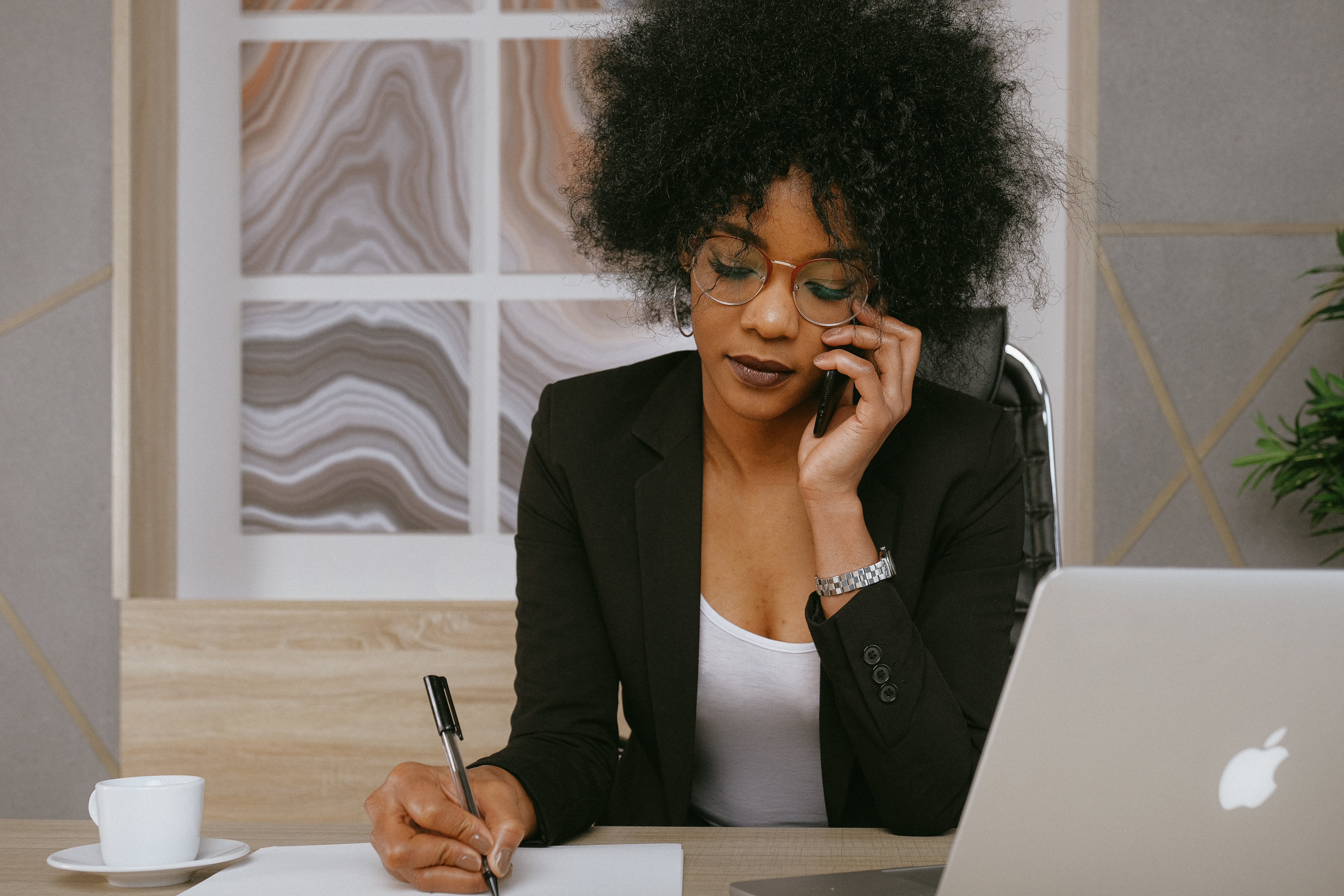 A hardworking woman on the phone while writing something down in her office | Source: Pexels