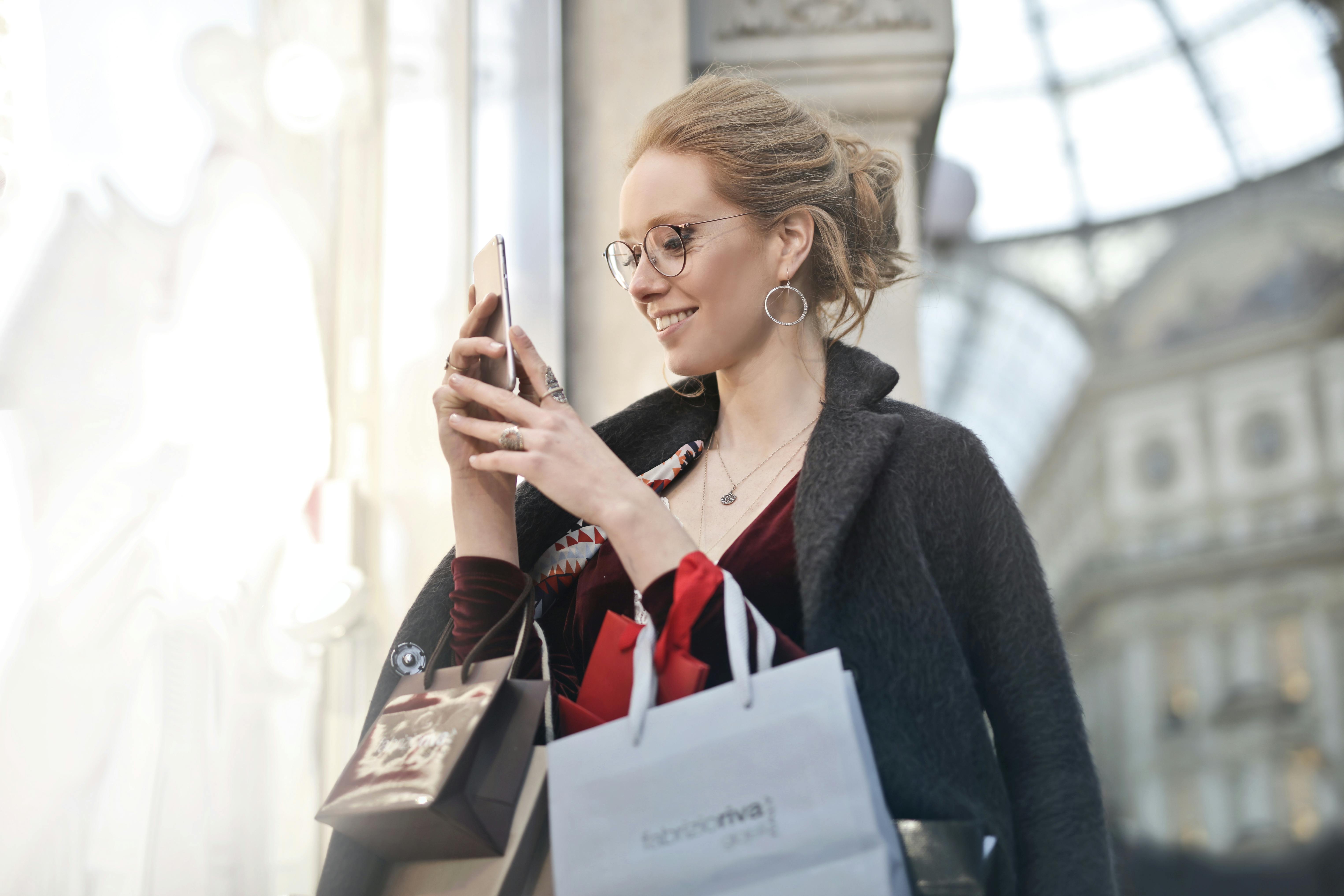 A woman smiling while holding several shopping bags while using at her phone | Source: Pexels