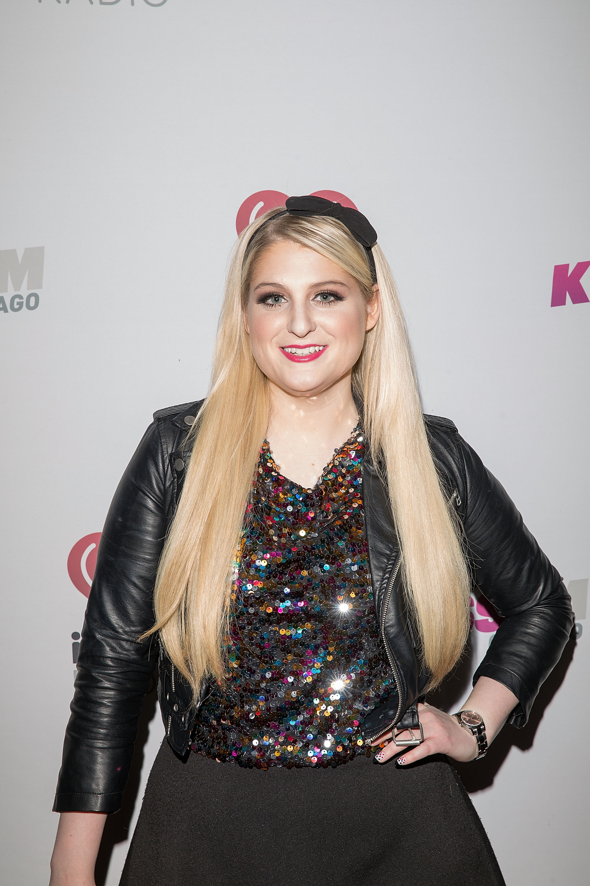 At 103.5 KISS FM's Jingle Ball 2014, Meghan Trainor rocks a sequined multicolored top under a black leather jacket, paired with sleek straight hair and a smile.