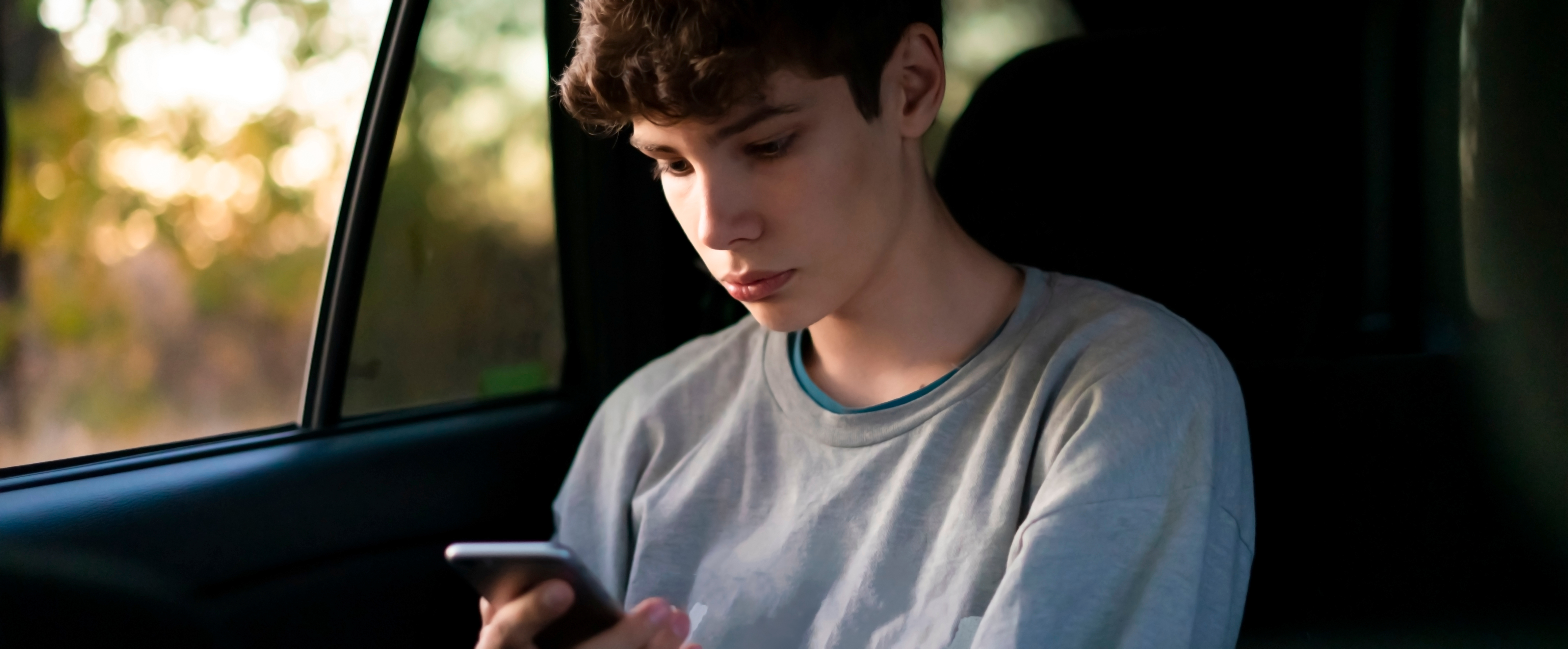 Young male passenger sitting on car back seat using a smartphone. | Source: Shutterstock