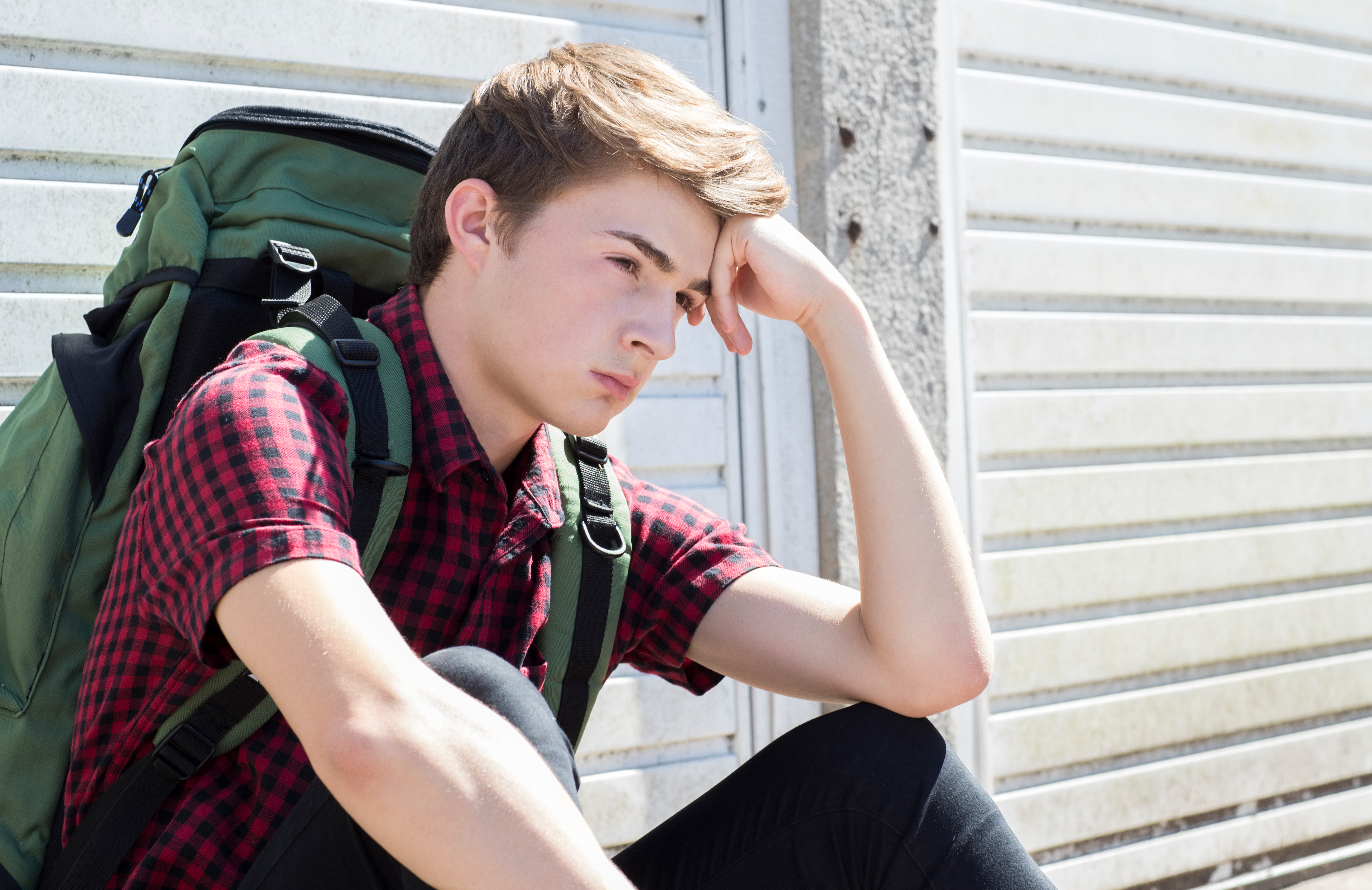 Ein gestresst aussehender Teenager mit Rucksack auf der Straße | Quelle: Shutterstock