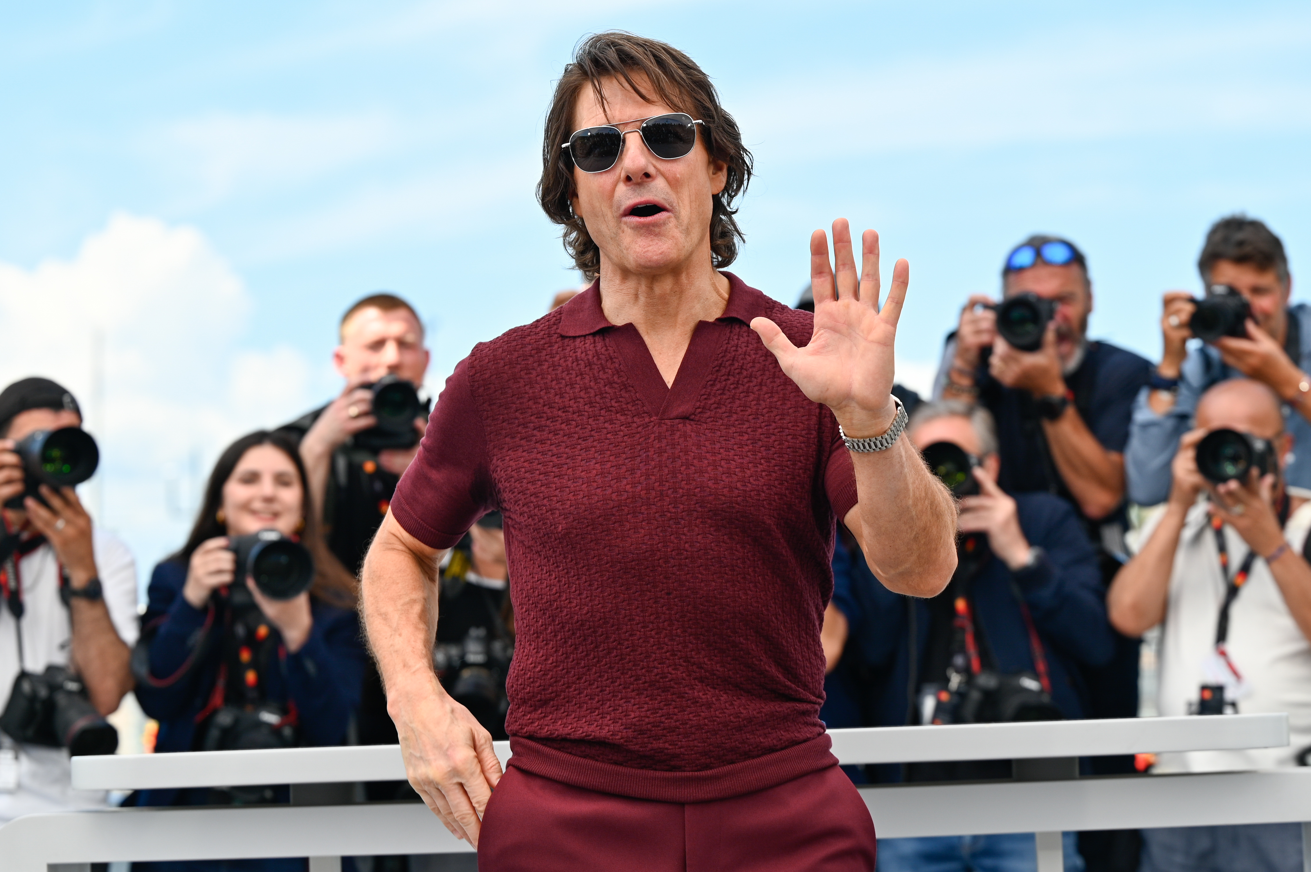 Tom Cruise greets the press with an animated wave during the "Mission: Impossible – The Final Reckoning" photocall in Cannes. His confident pose and lively expression drew plenty of camera flashes.