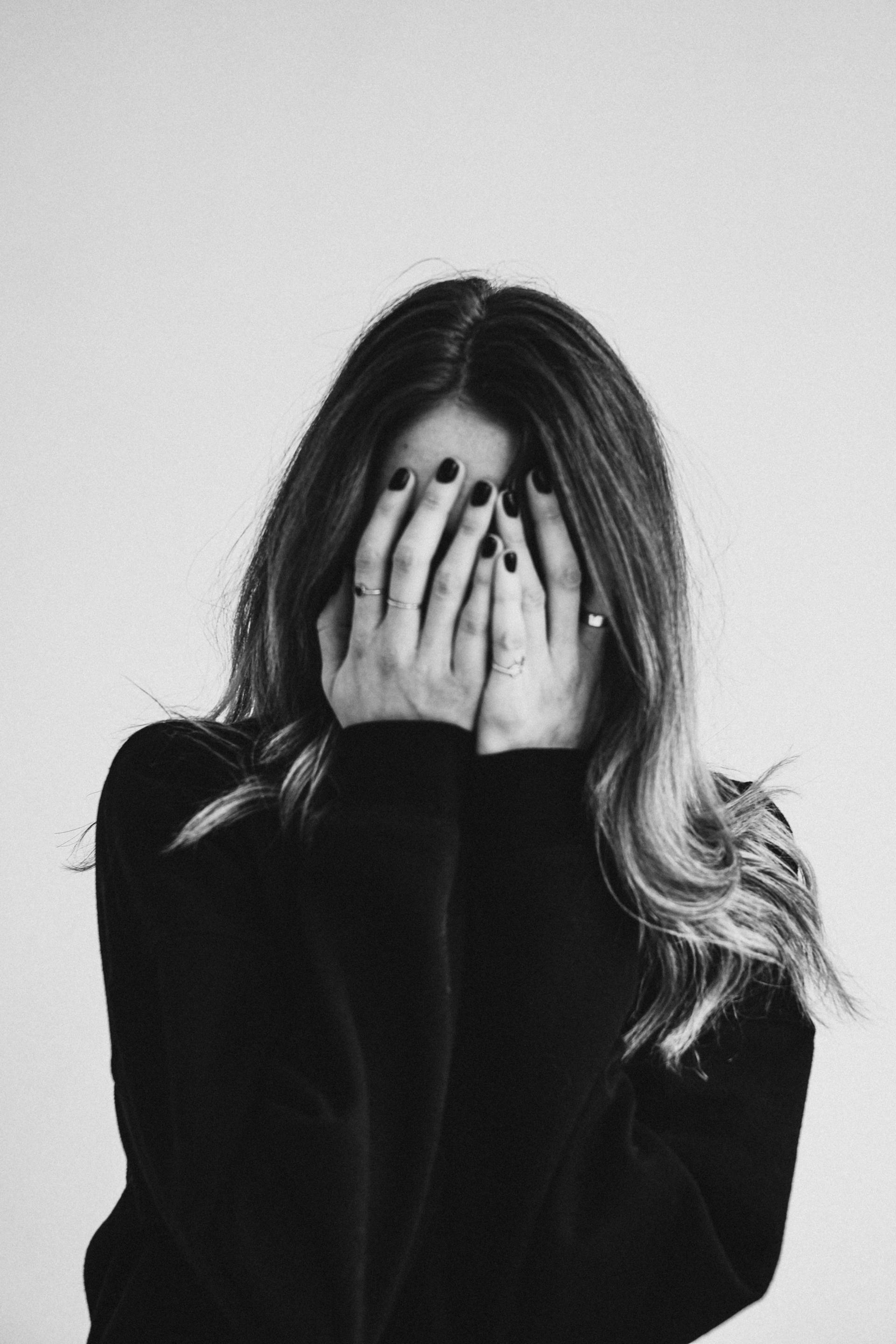 Grayscale photo of a young woman covering her face | Source: Pexels