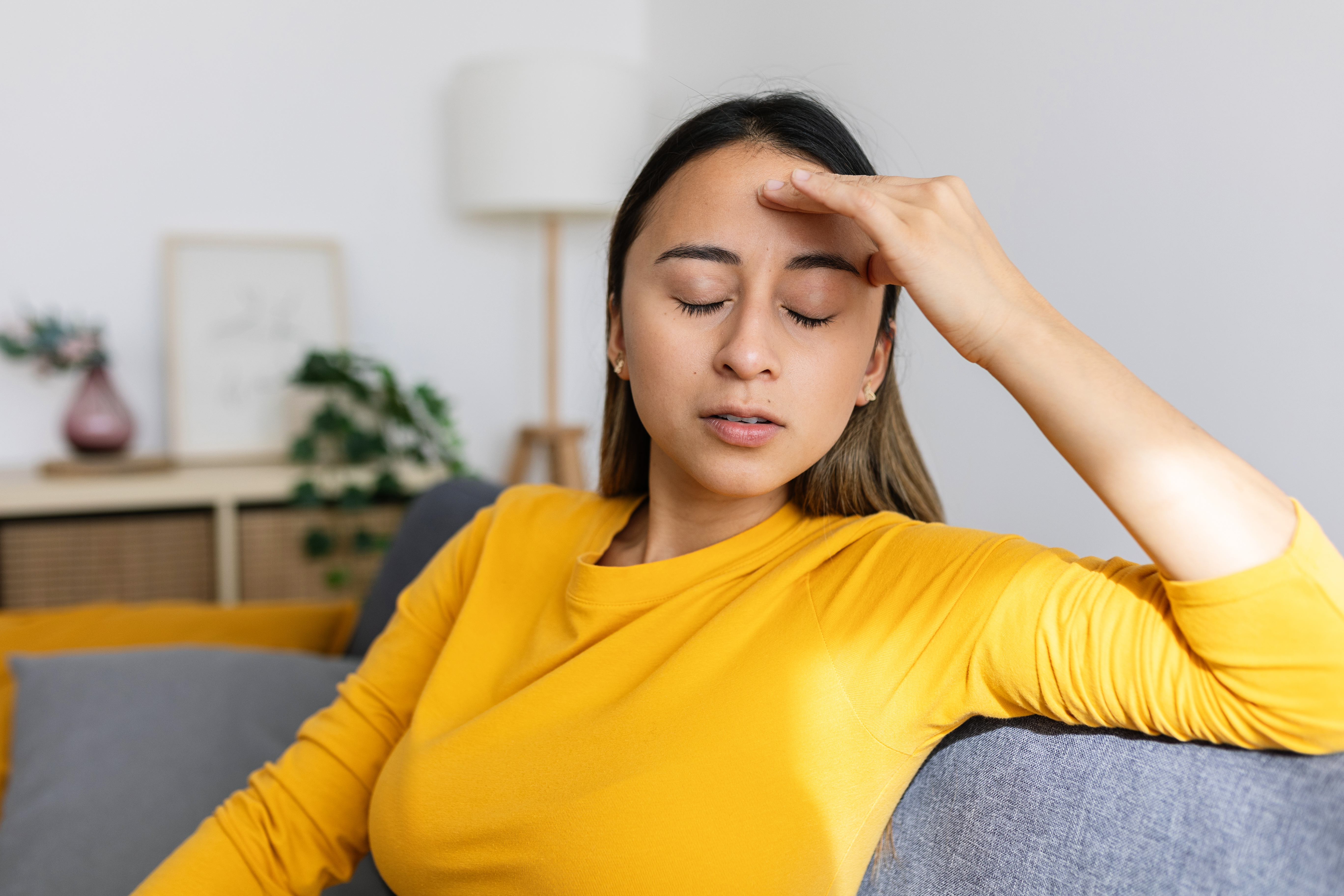 Frustrated young woman feeling tired and worried about problem sitting on sofa at home. Stressed or depressed girl having bad emotions | Source: Getty Images