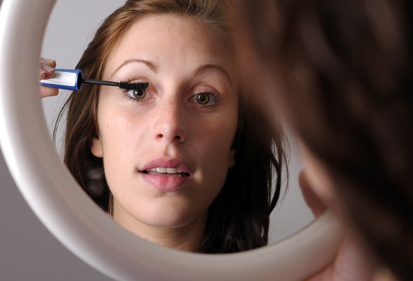  jeune femme se maquillant devant un miroir.|Photo : Getty Images