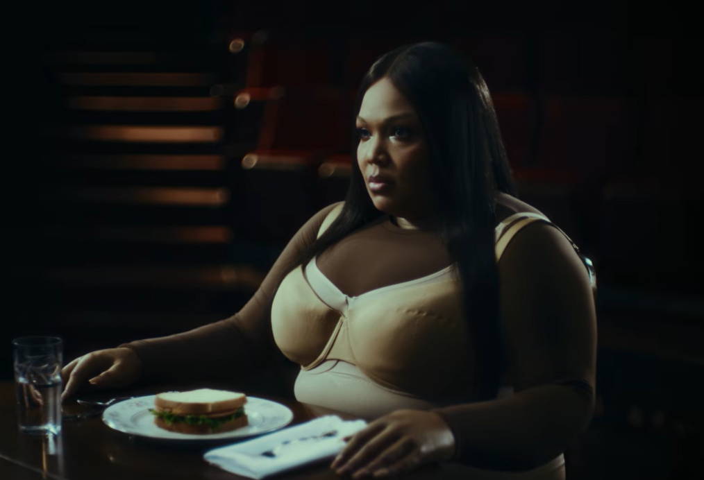 The two versions sit across from each other at a quiet dinner table | Source: YouTube/Lizzo