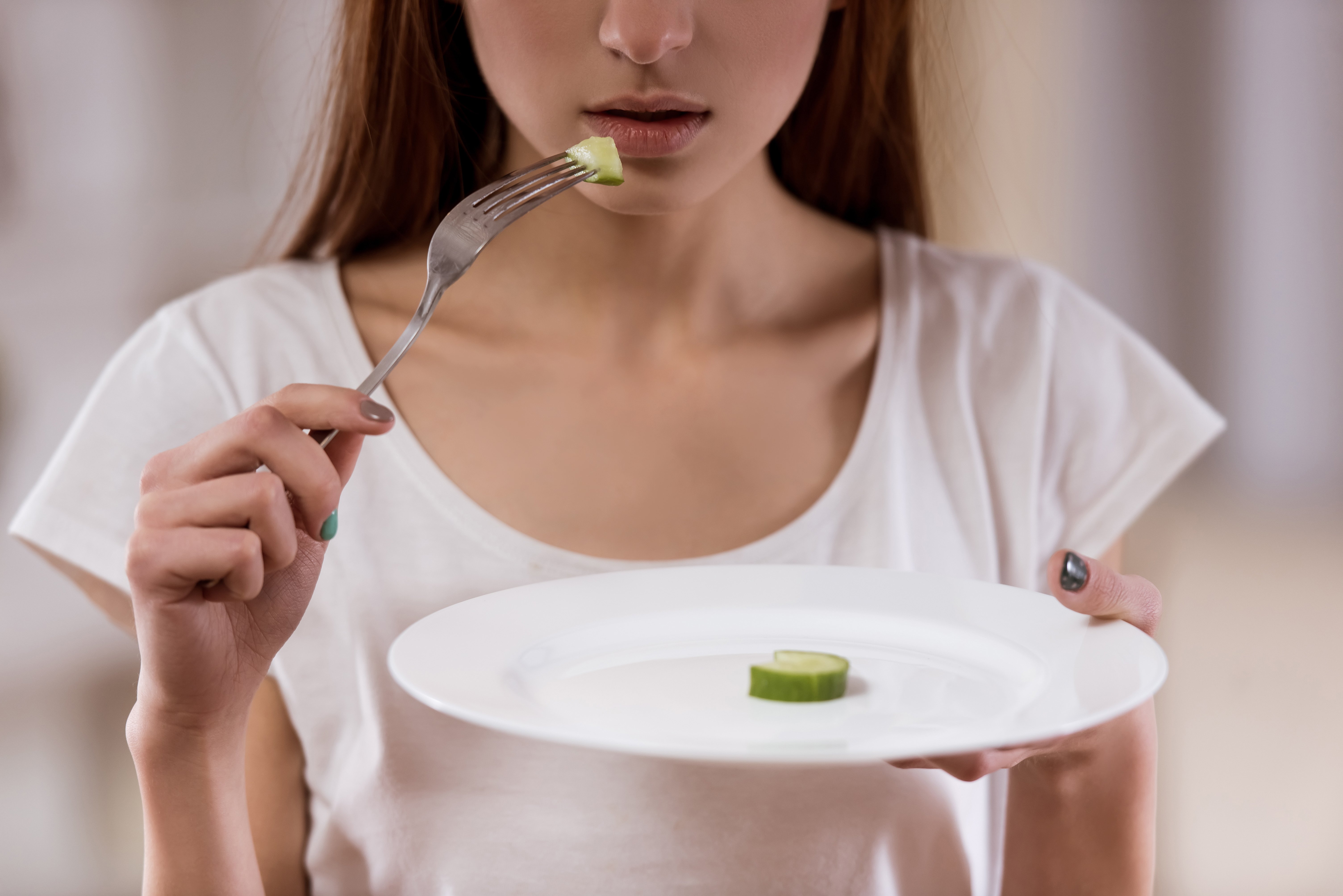 Chica delgada con un plato vacío de pie en el centro de la habitación. Fuente: Shutterstock Chica delgada con un plato vacío de pie en el centro de la habitación. Fuente: Shutterstock