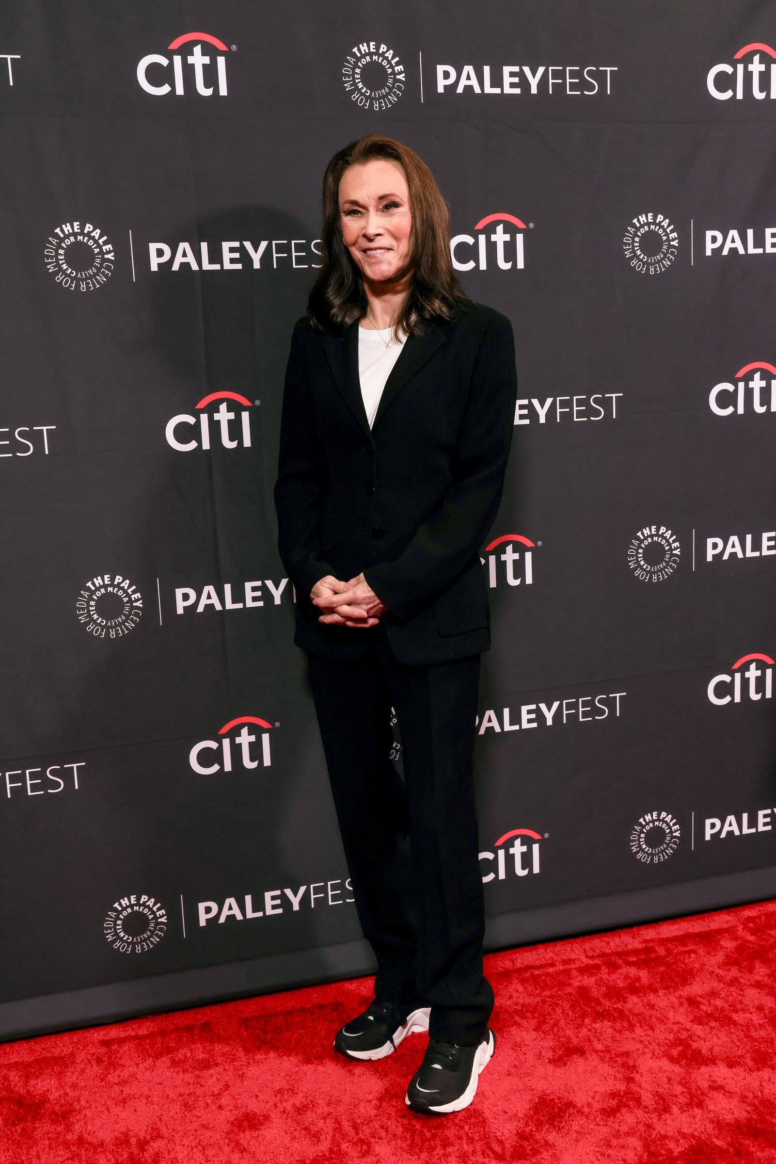 Kate Jackson stands on the red carpet at PaleyFest LA, wearing a tailored dark suit and sneakers, blending classic elegance with a relaxed, modern style.