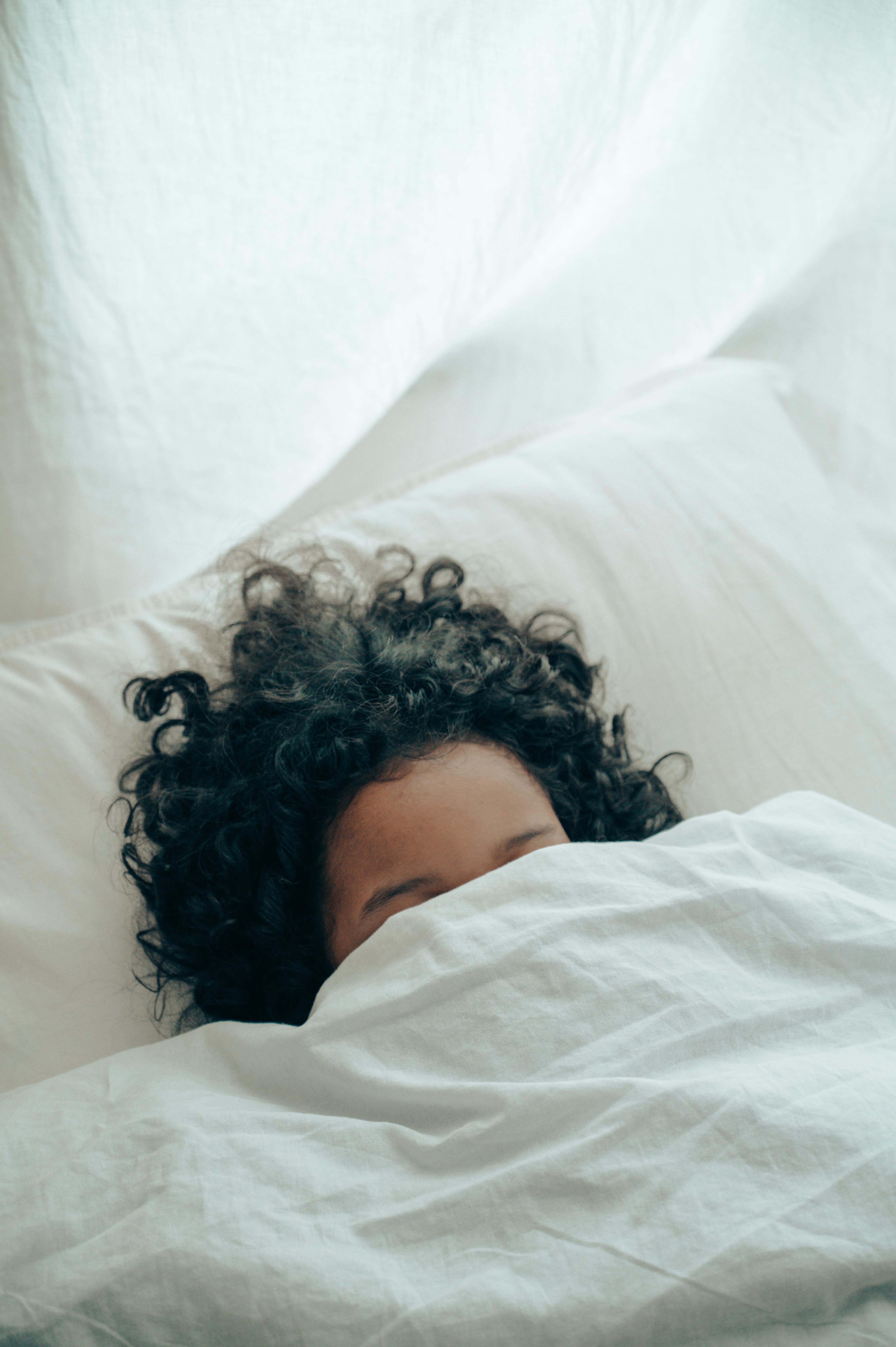 A child in bed ducking under the duvet | Source: Pexels