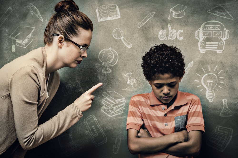 Angry teacher scolding student in front of the classroom. | Photo: Shutterstock.