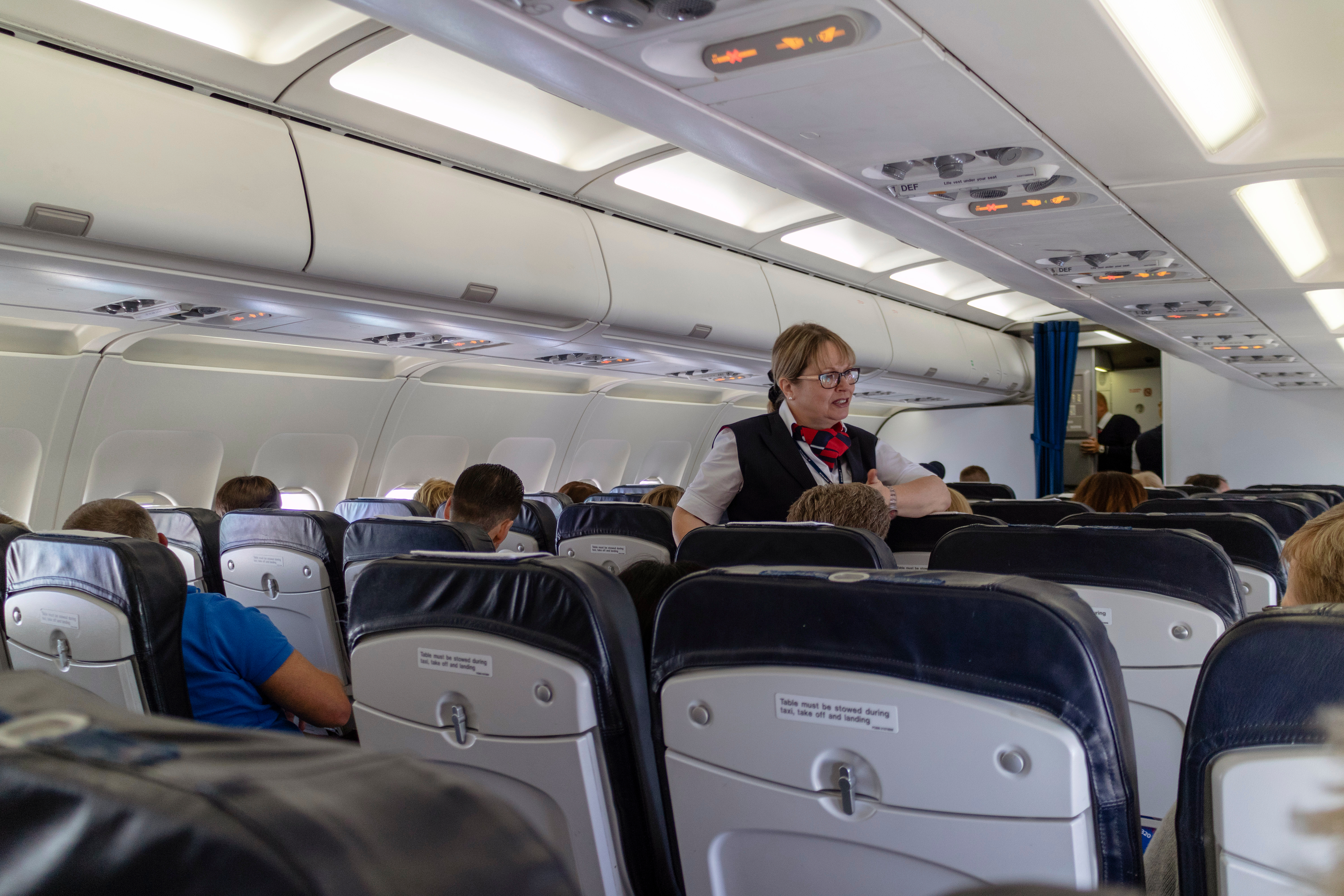 Inflight service on a passenger plane with a crew member speaking to a passenger | Source: Shutterstock