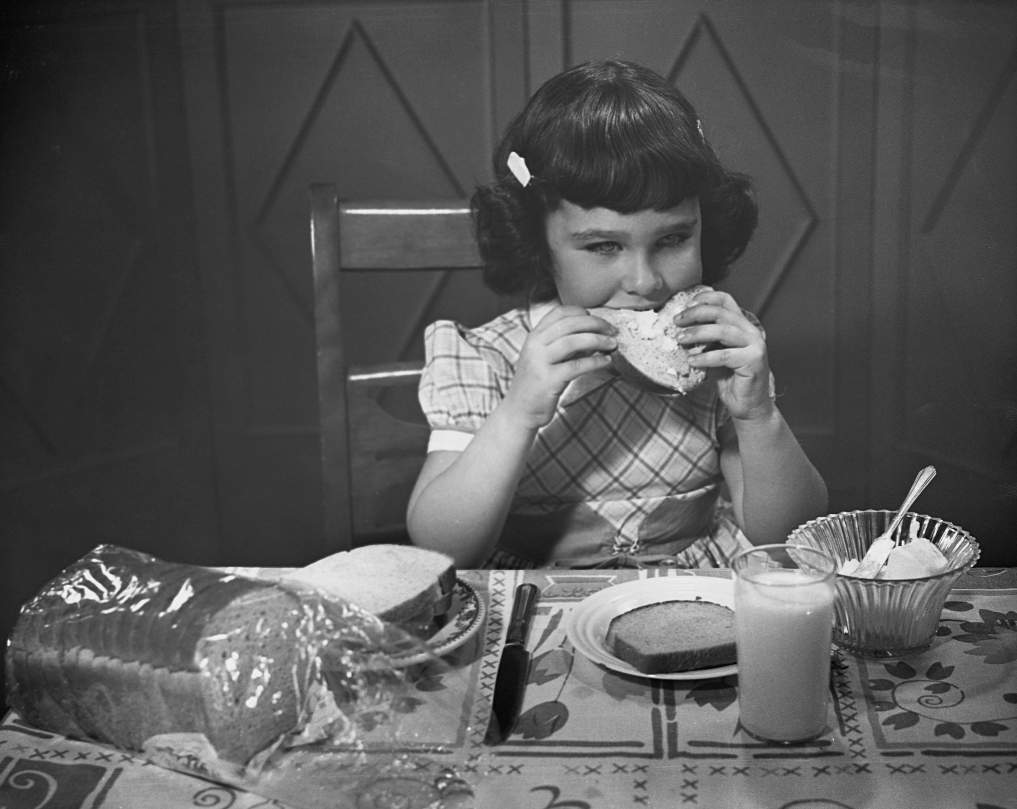 A little girl eats a slice of buttered toast in the 1950s.| Source: Getty Images 