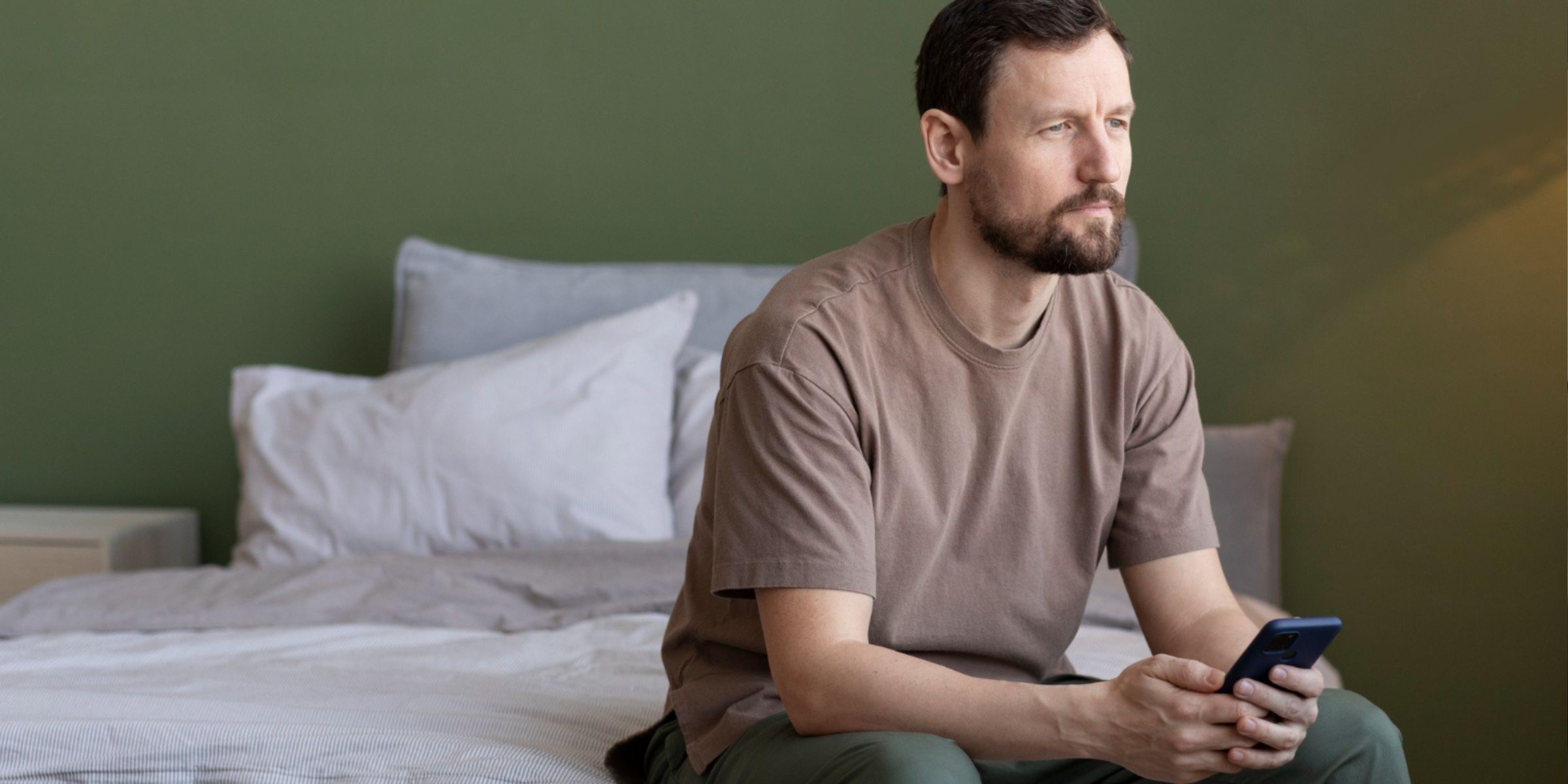 A man holding his phone and sitting on the bed | Source: Freepik