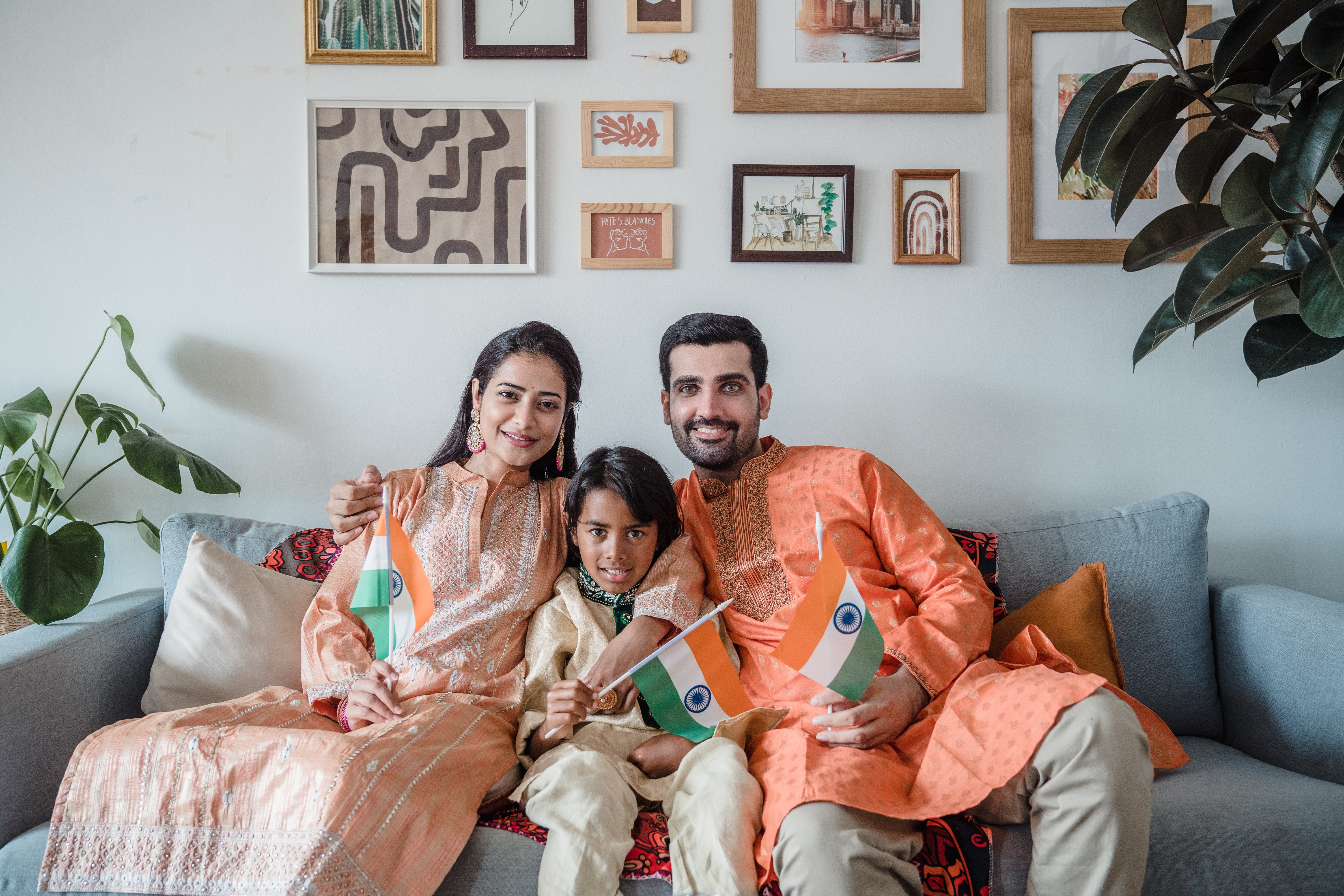 A happy family of three sitting on a couch holding their country's flag | Source: Pexels