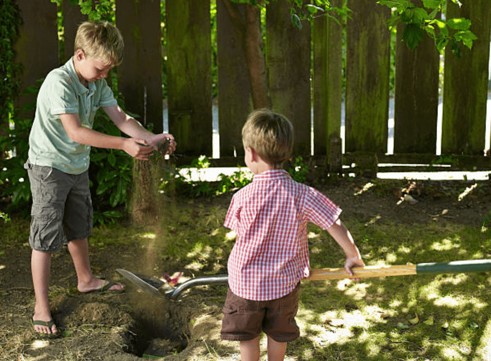 Two young boys help each other to bury a pet in their backyard | Source: Getty Images