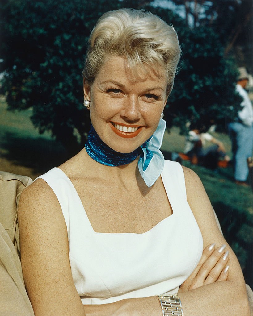 Hollywood actress Doris Day beams, wearing a white outfit paired pearl earrings and a blue scarf in 1955. / Source: Getty Images