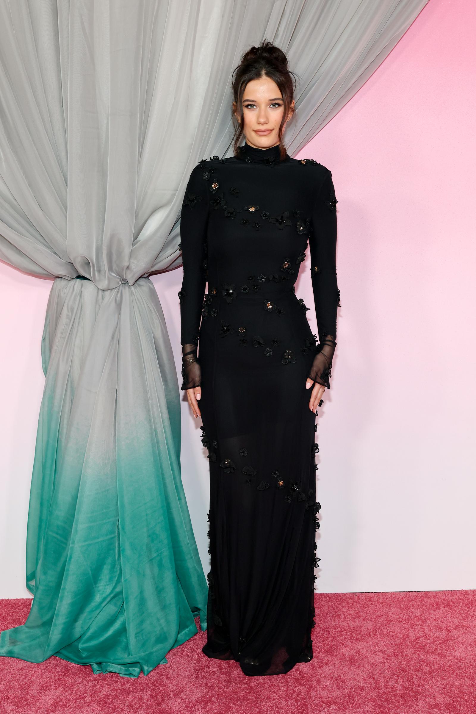 Ella Bleu Travolta wears a fitted black gown with sheer gloves at the 2026 Fashion Trust U.S. Awards in Los Angeles. The elegant look underscores her style evolution from celebrity child to fashion-forward young woman.
