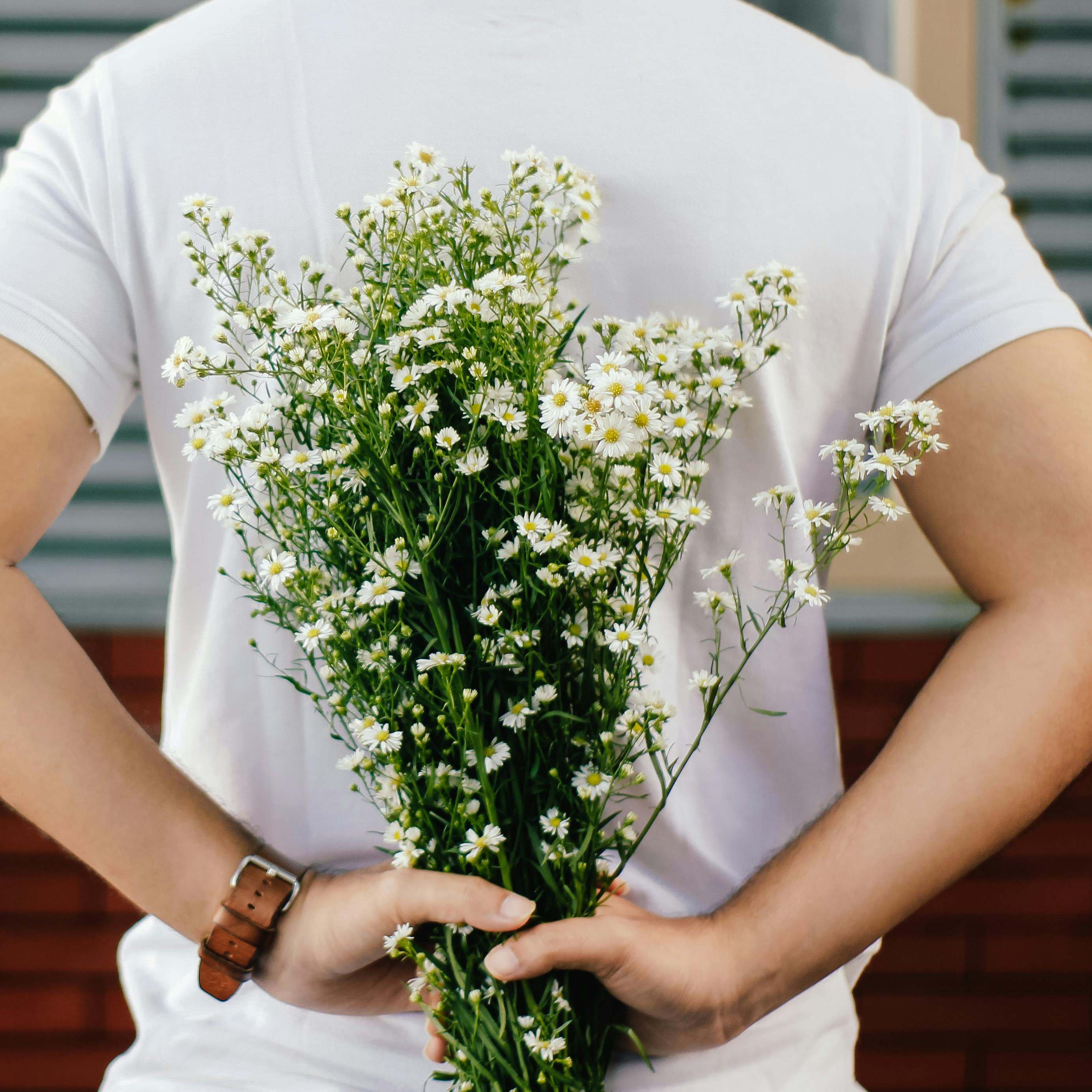 A man holding a bunch of flowers behind his back | Source: Pexels