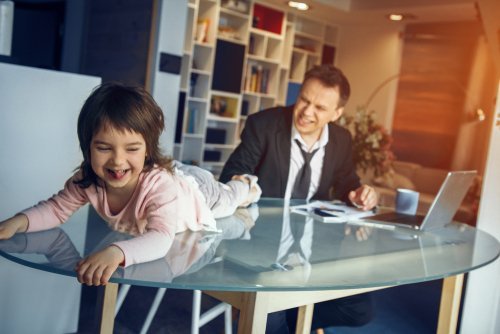 Young daughter playing on the table while her father tries to work. | Source: Shutterstock.