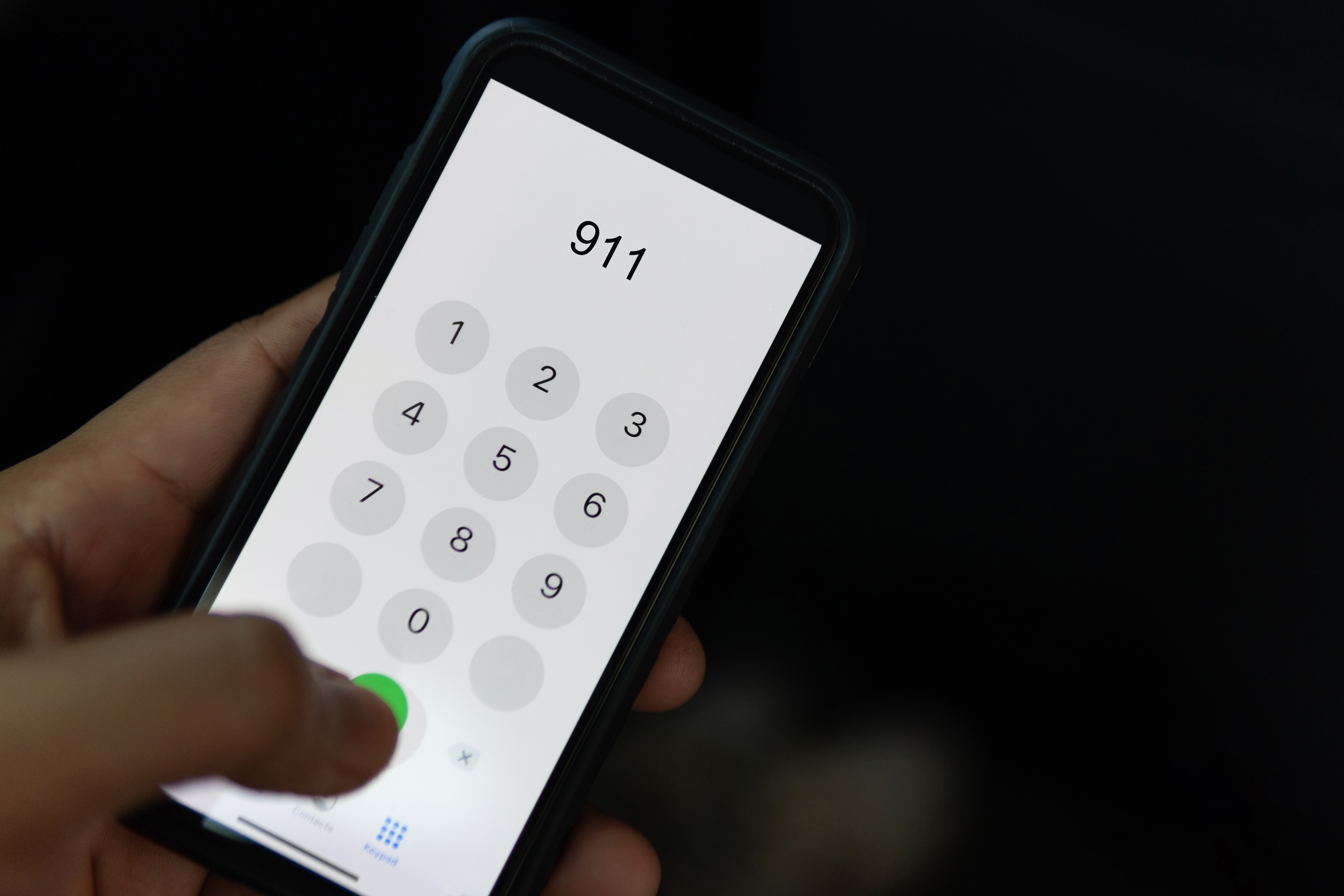 Hand holding cell phone with emergency number 911 on black background. | Source: Shutterstock