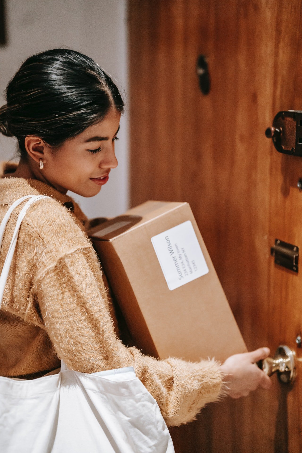 Una mujer con una gran caja en sus brazos, abre la puerta de la casa. | Foto: Pexels