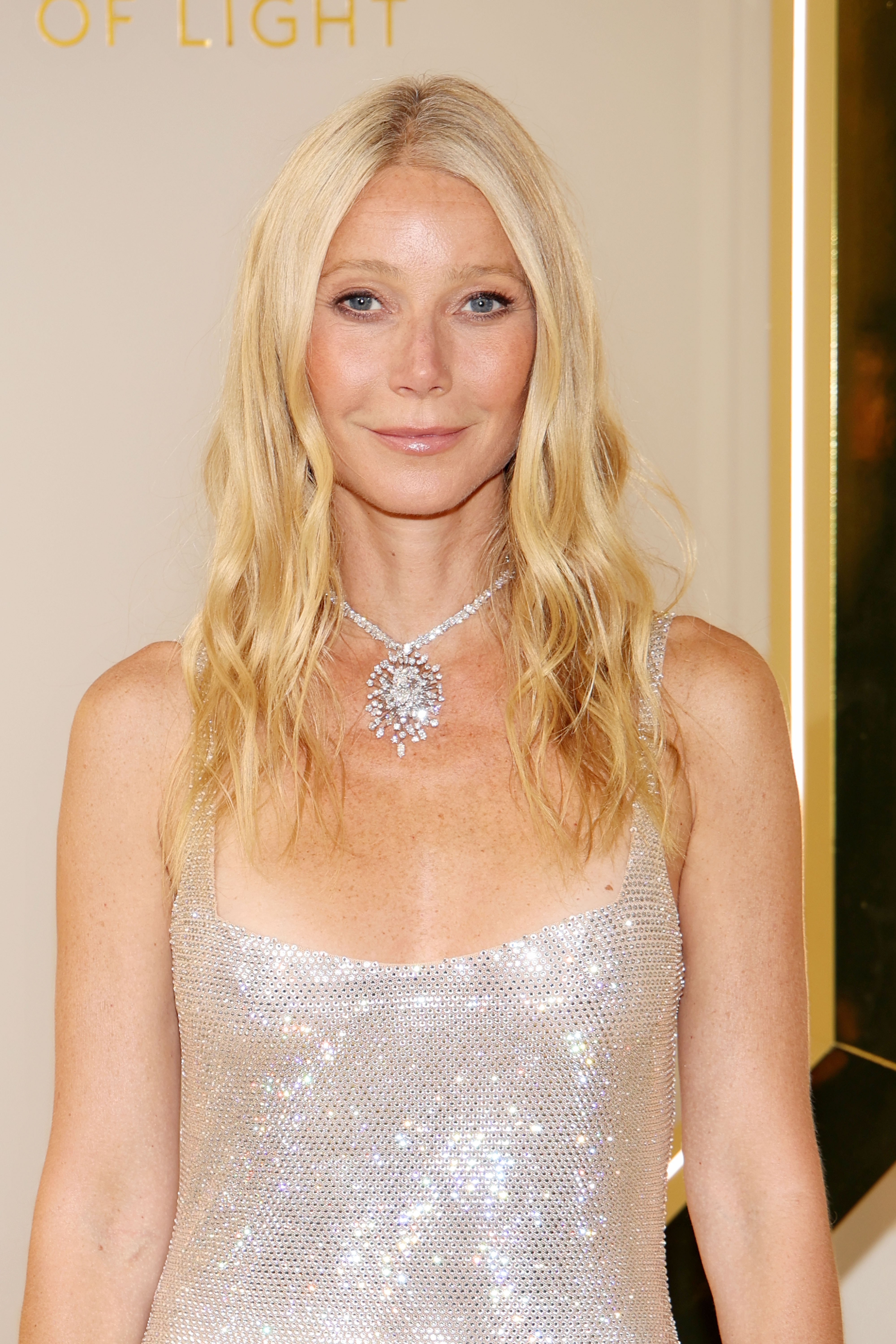 Gwyneth Paltrow poses front-facing at Milan Fashion Week on June 16, 2024, wearing a shimmering silver dress and statement necklace, her hair parted center and falling straight.