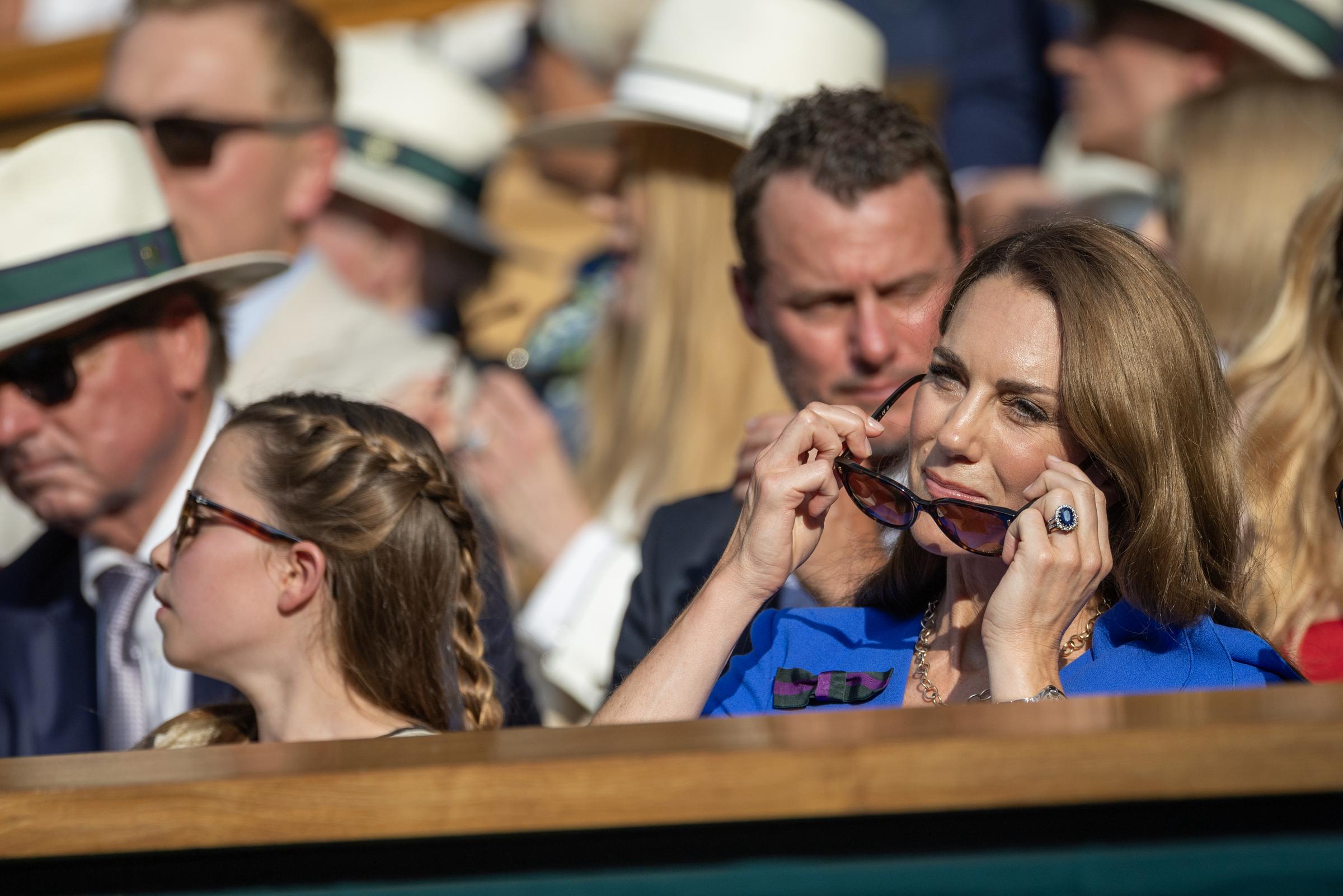 Princess Charlotte and Princess Catherine sit side by side in the Royal Box during the Gentlemen’s Singles Final at Wimbledon. Catherine adjusts her sunglasses while Charlotte looks on attentively amid the crowd.