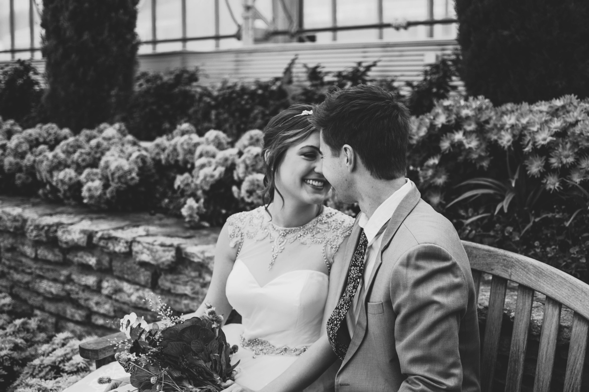 Grayscale shot of a happy bride and groom sitting on a wooden bench | Source: Unsplash