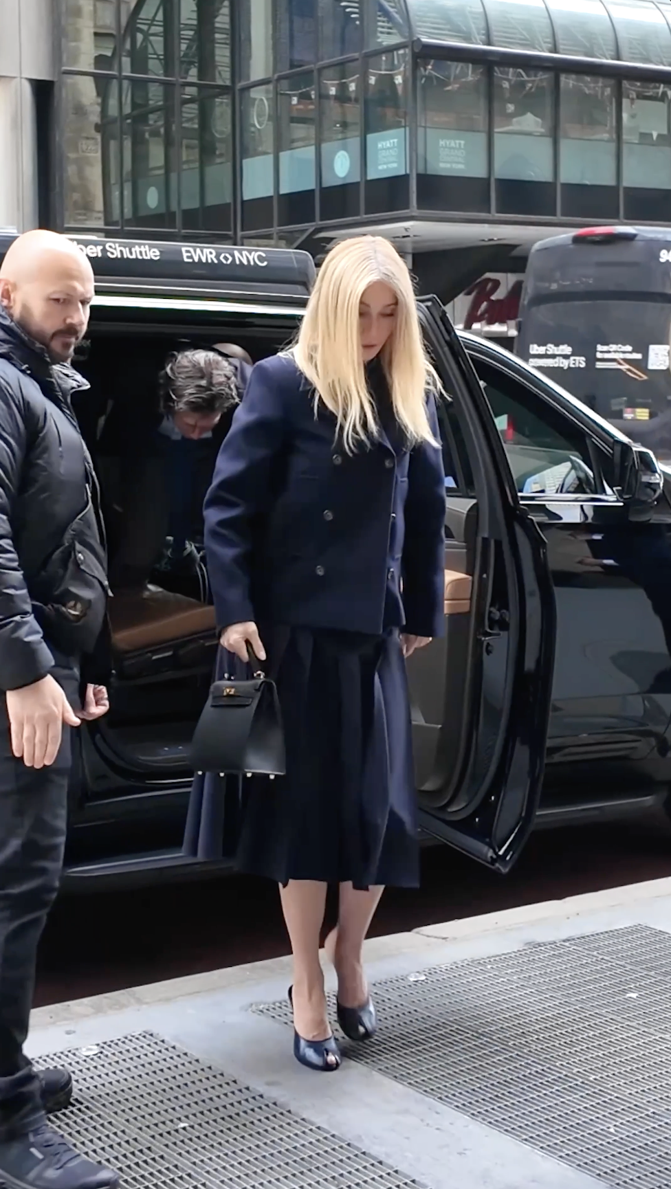 Gwyneth Paltrow walks forward after stepping out in New York City, holding a black Hermès Kelly bag, her pleated skirt moving subtly with each step.
