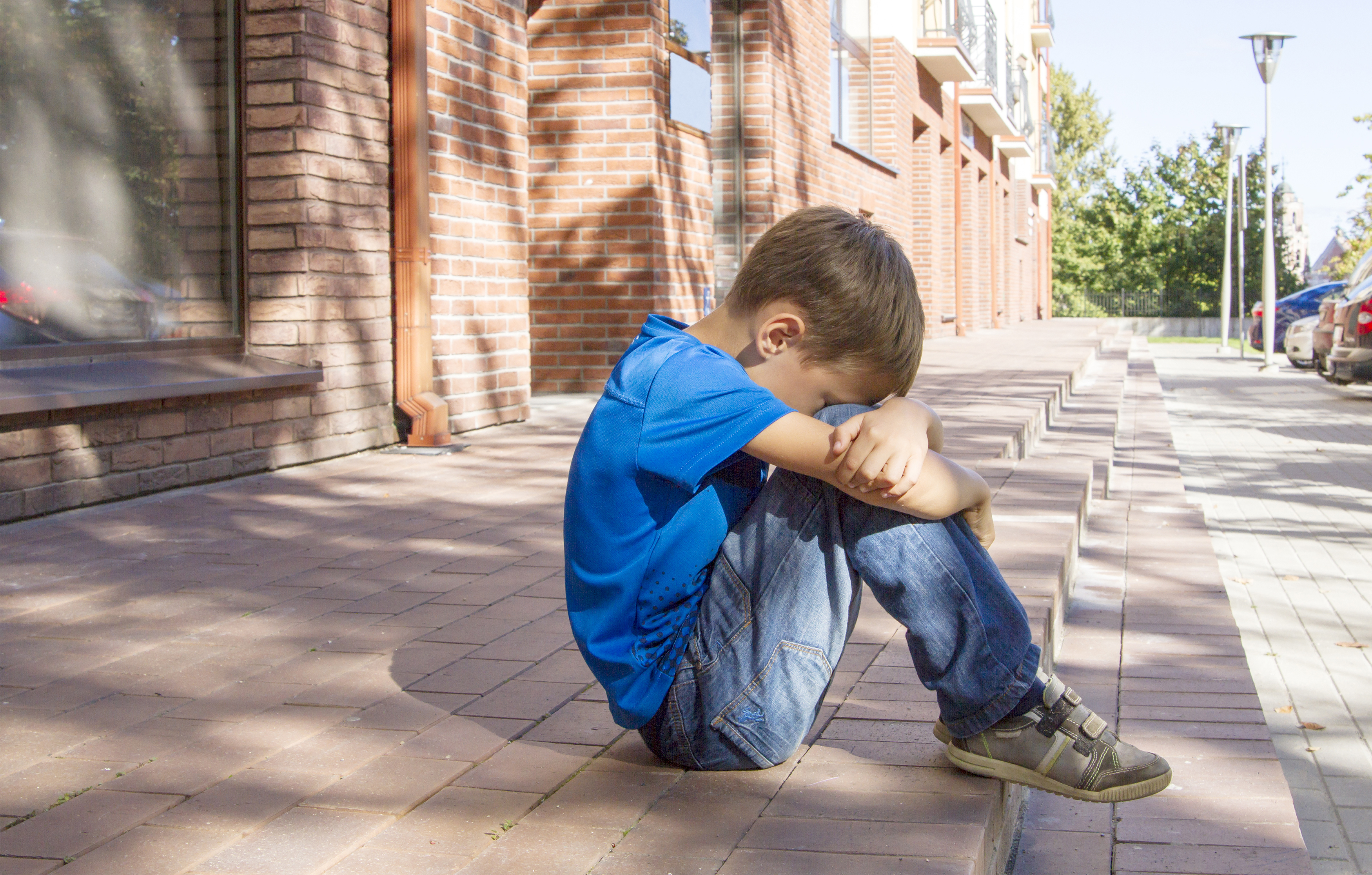 A sad young boy sitting on a sidewalk | Source: Shutterstock