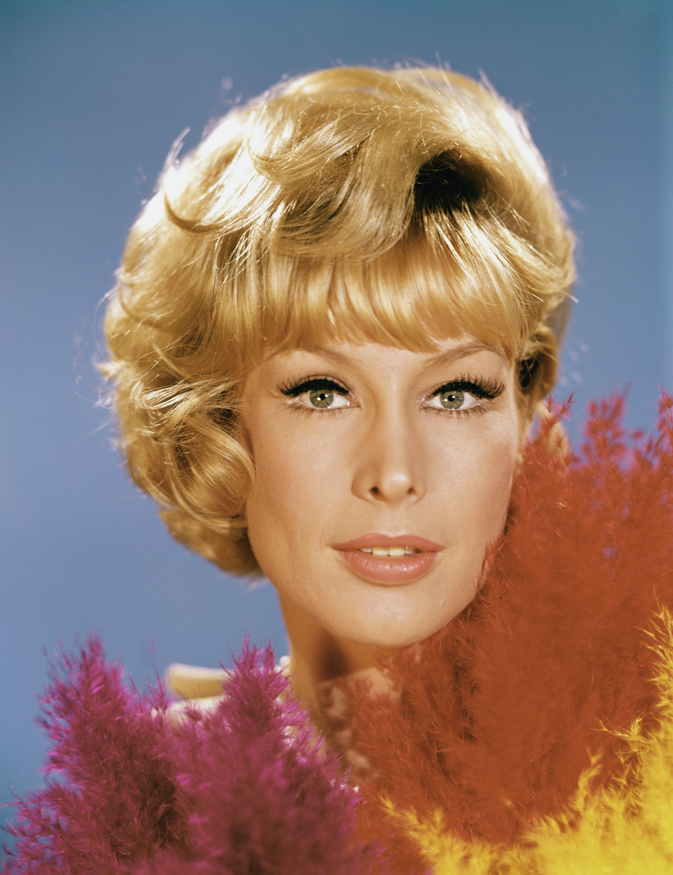 Barbara Eden appears as Jeannie with a polished blond bob, dramatic eye makeup, and colorful feathers framing her face in this "I Dream of Jeannie" Season one portrait.