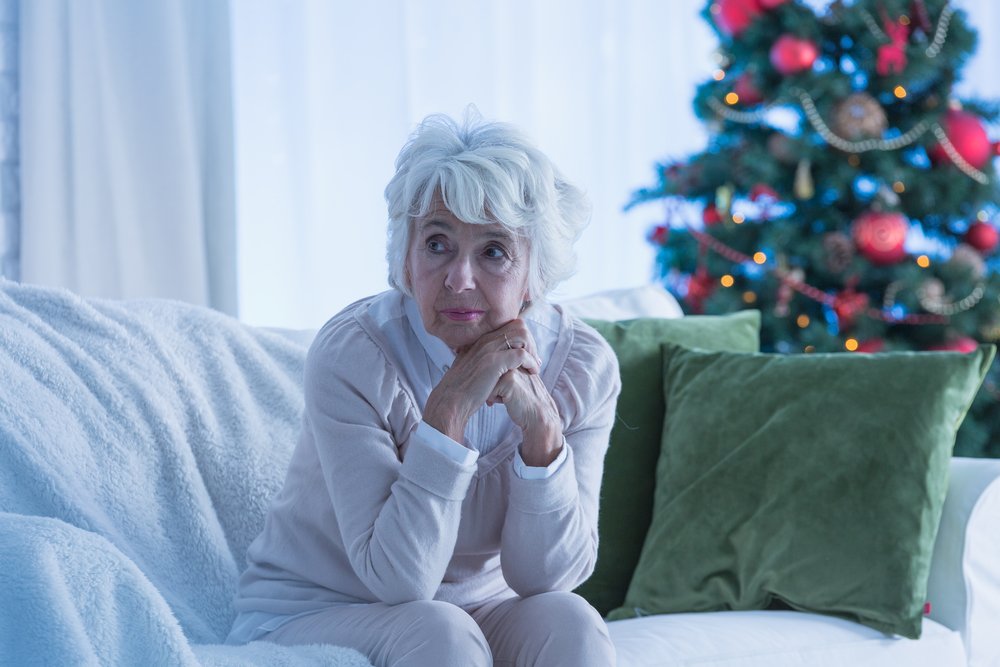 Anciana pensativa sentada en un sofá con un arbol de Navidad en el fondo. | Foto: Shutterstock  