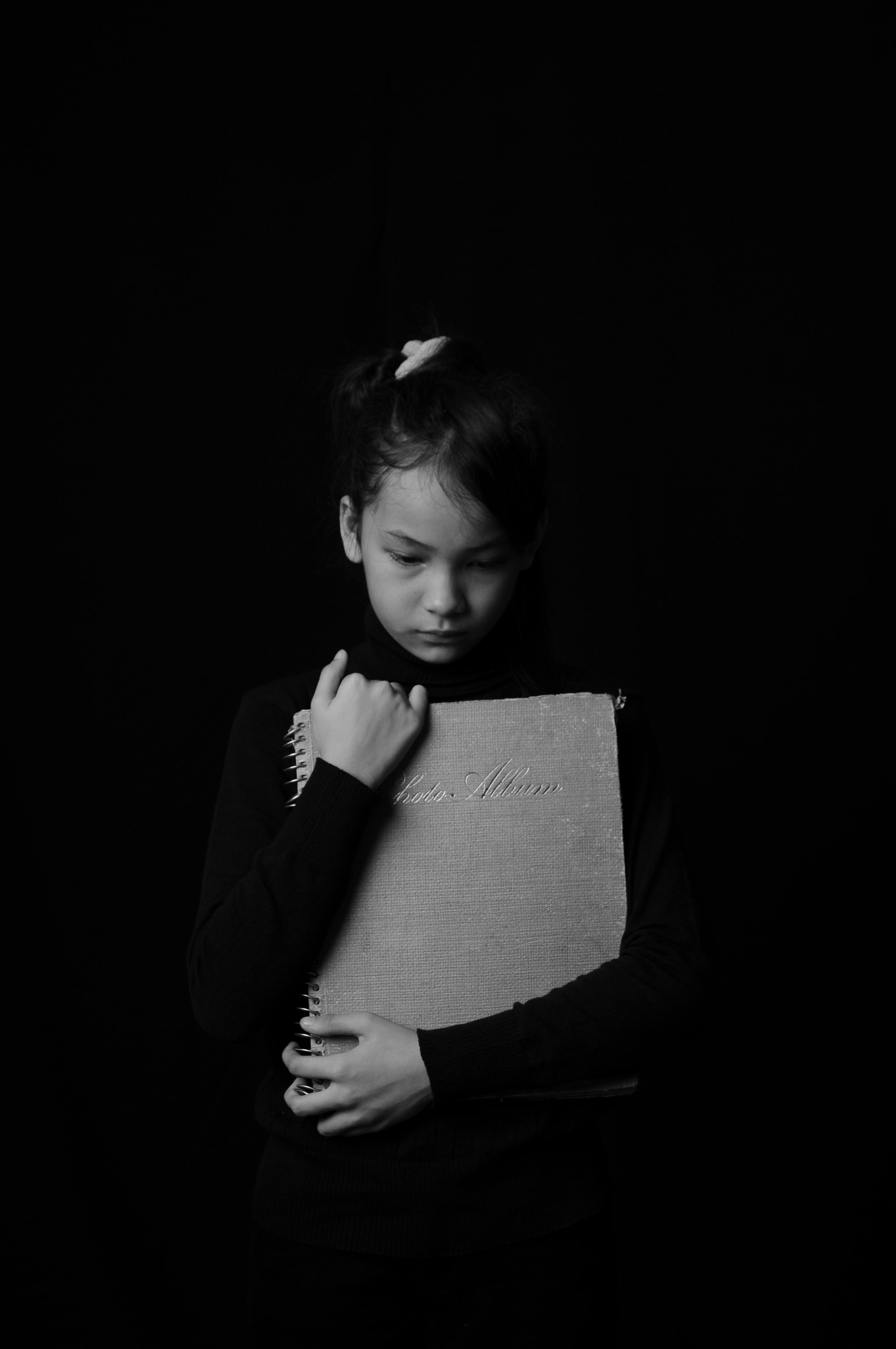 A sad girl child holding a photo album | Source: Pexels